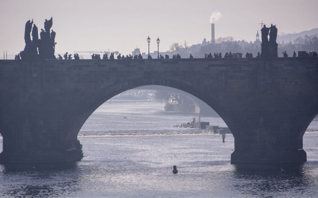 Silhouetten von Menschen auf der Karlsbrücke mit Blick durch einen Brückenbogen auf die Moldau