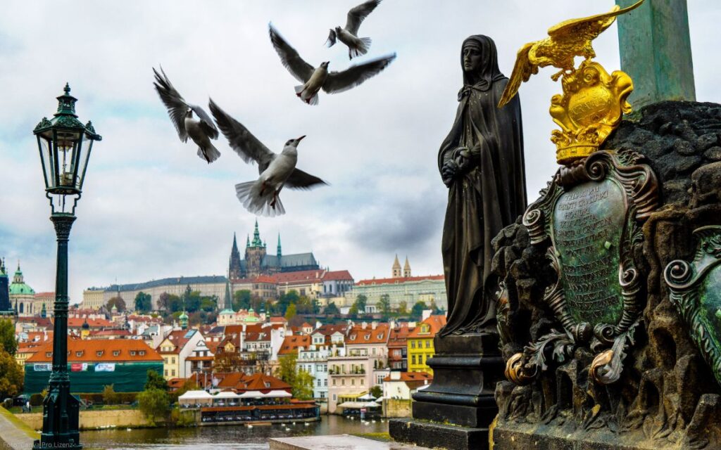 Tauben fliegen vor Statuen auf der Karlsbrücke mit Blick auf die Prager Burg