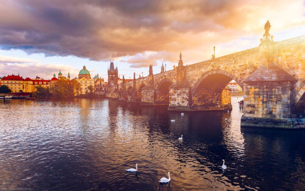 Karlsbrücke bei Sonnenuntergang mit warmen Wolkenfarben und Schwänen auf der Moldau