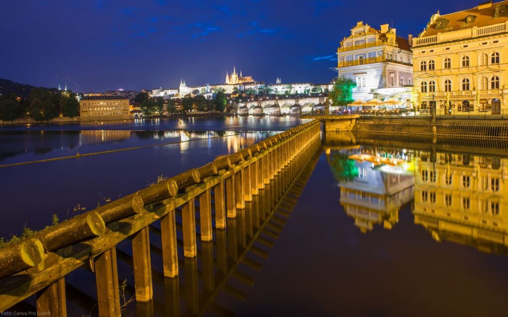 Beleuchtete Moldau mit Holzbarrieren und Blick auf die Prager Burg