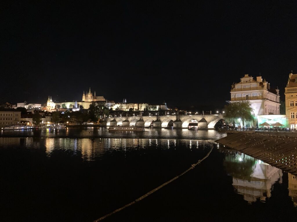 Nachtaufnahme der Karlsbrücke und Prager Burg mit Spiegelungen auf der Moldau