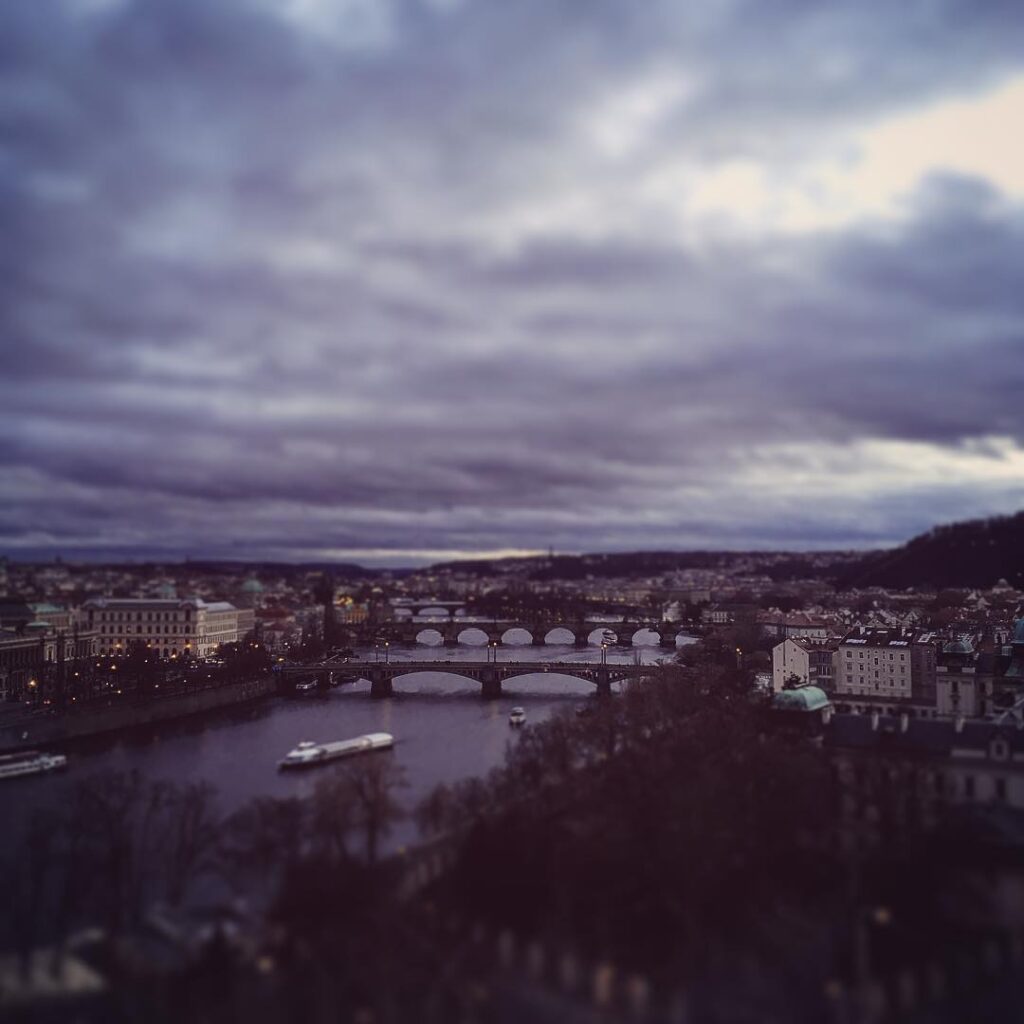 Panoramaaufnahme mit mehreren Brücken über die Moldau unter einem wolkenverhangenen Winterhimmel. Das Bild zeigt die Tiefe und Struktur des Prager Flusstals.