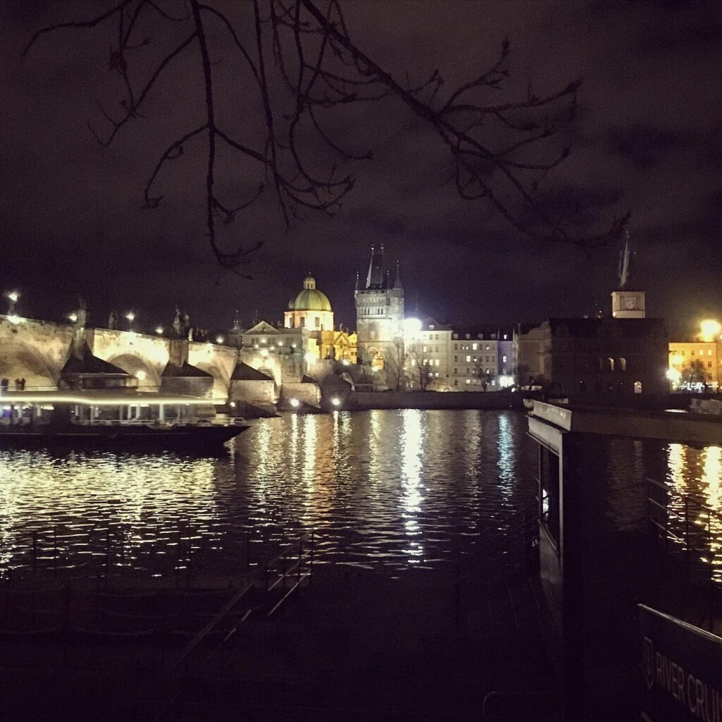 Nachtaufnahme der Moldau und der beleuchteten Altstadt. Die Reflexionen im Wasser verstärken die ruhige Atmosphäre des Abends.
