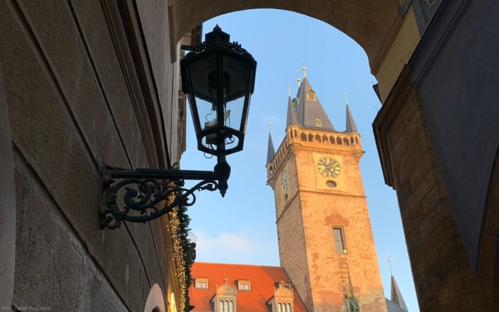 Blick durch einen Torbogen auf den Rathausturm am Altstädter Ring in Prag mit Uhr und historischer Laterne im Vordergrund