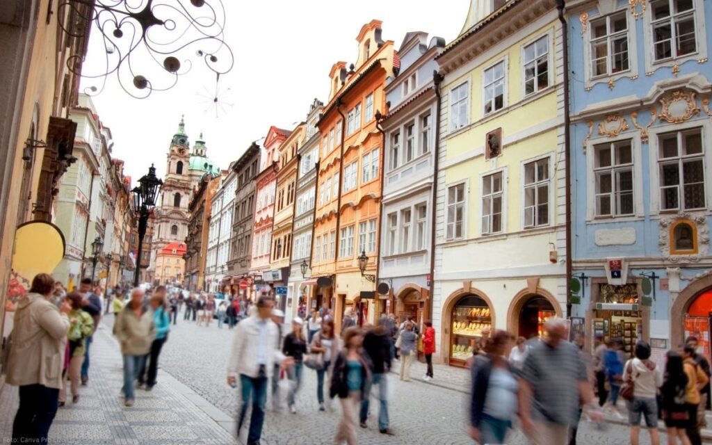 Belebte Straße auf der Prager Kleinseite mit historischen Häuserfassaden und Blick zur St.-Nikolaus-Kirche