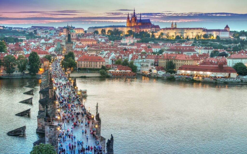 Blick über die Karlsbrücke in Prag mit Menschen, der Moldau und der beleuchteten Prager Burg im Hintergrund
