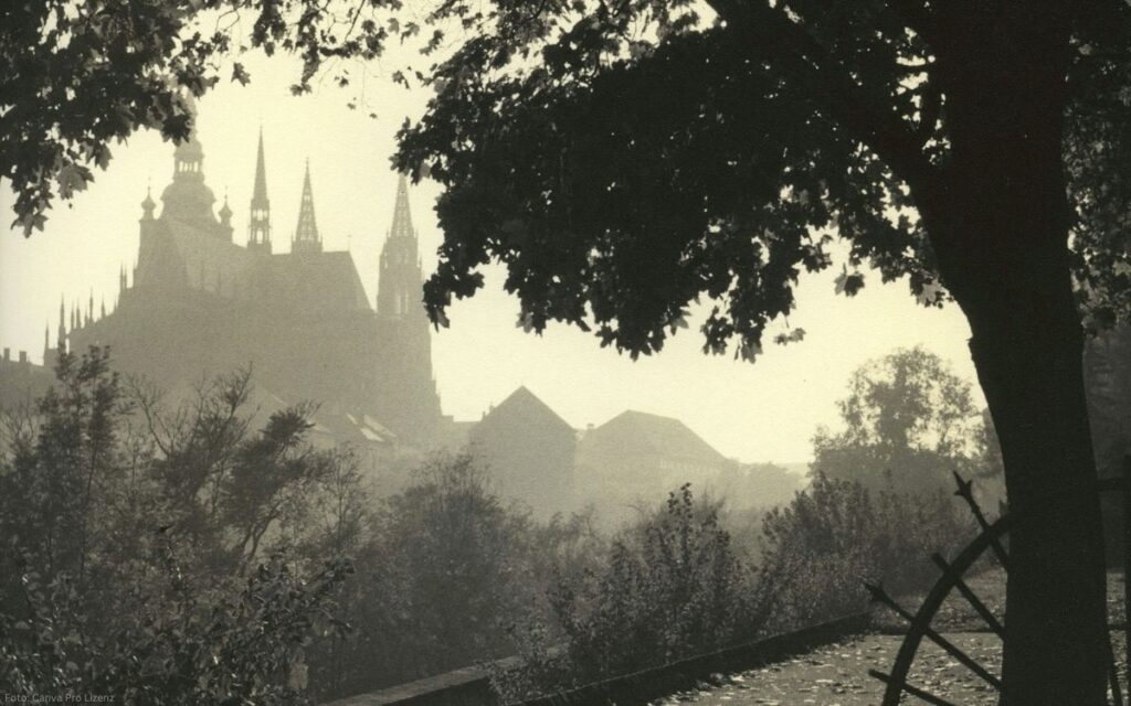 Prager Burg mit Veitsdom im morgendlichen Nebel, eingerahmt von Bäumen und Parklandschaft