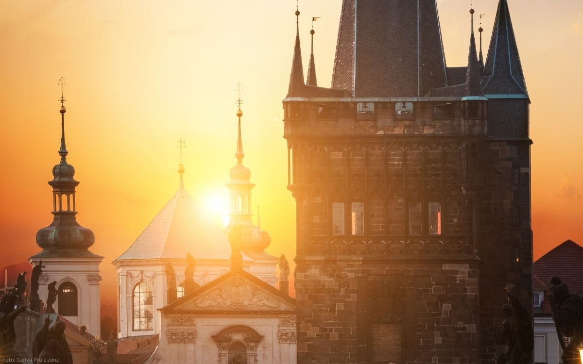 Sonnenaufgang über der Prager Altstadt mit dem Altstädter Brückenturm an der Karlsbrücke und barocken Türmen im warmen Morgenlicht