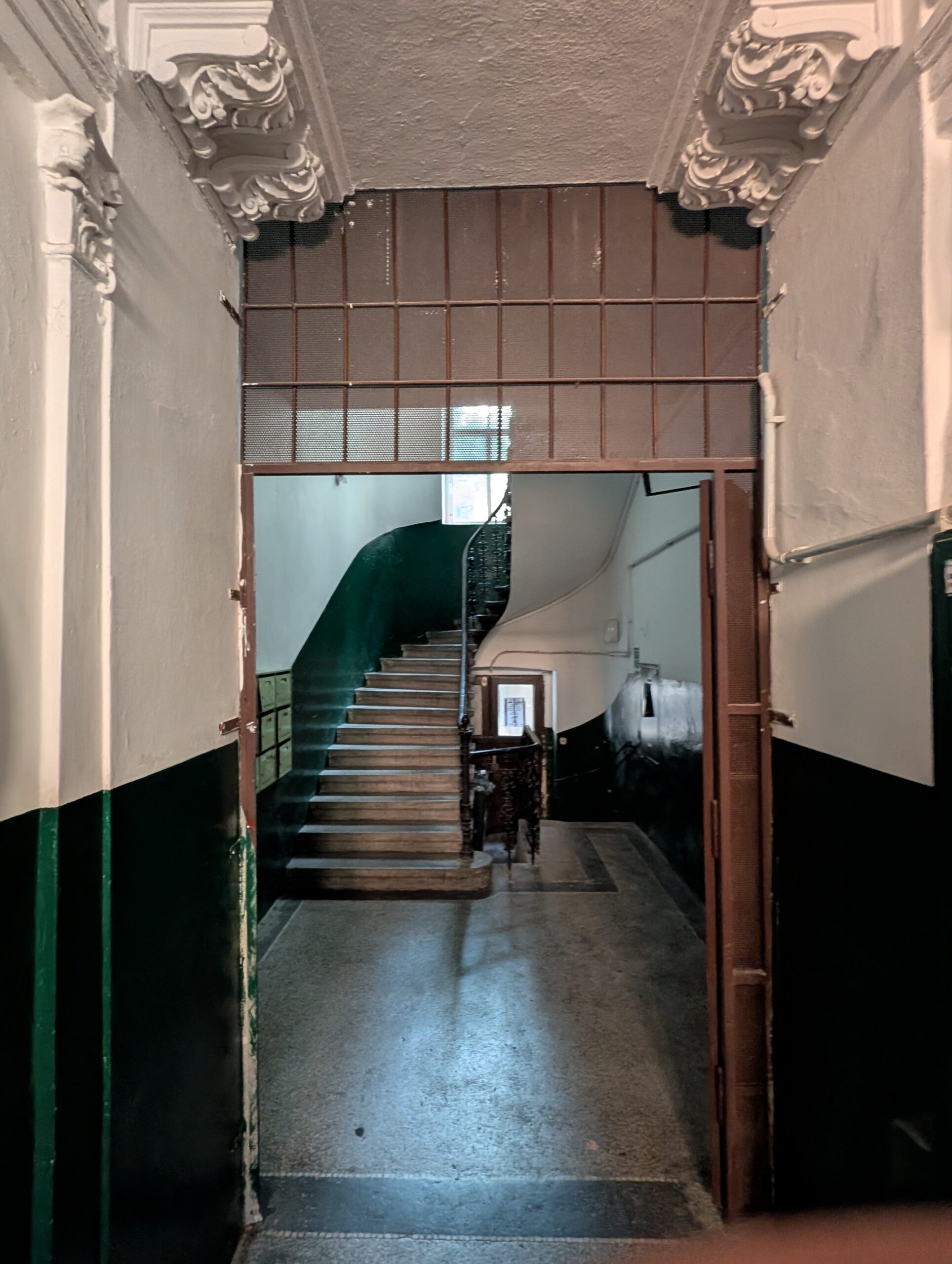 Historisches Treppenhaus in Prag mit Metalltor, geschwungener Treppe, grün gestrichenen Wänden und Stuckelementen