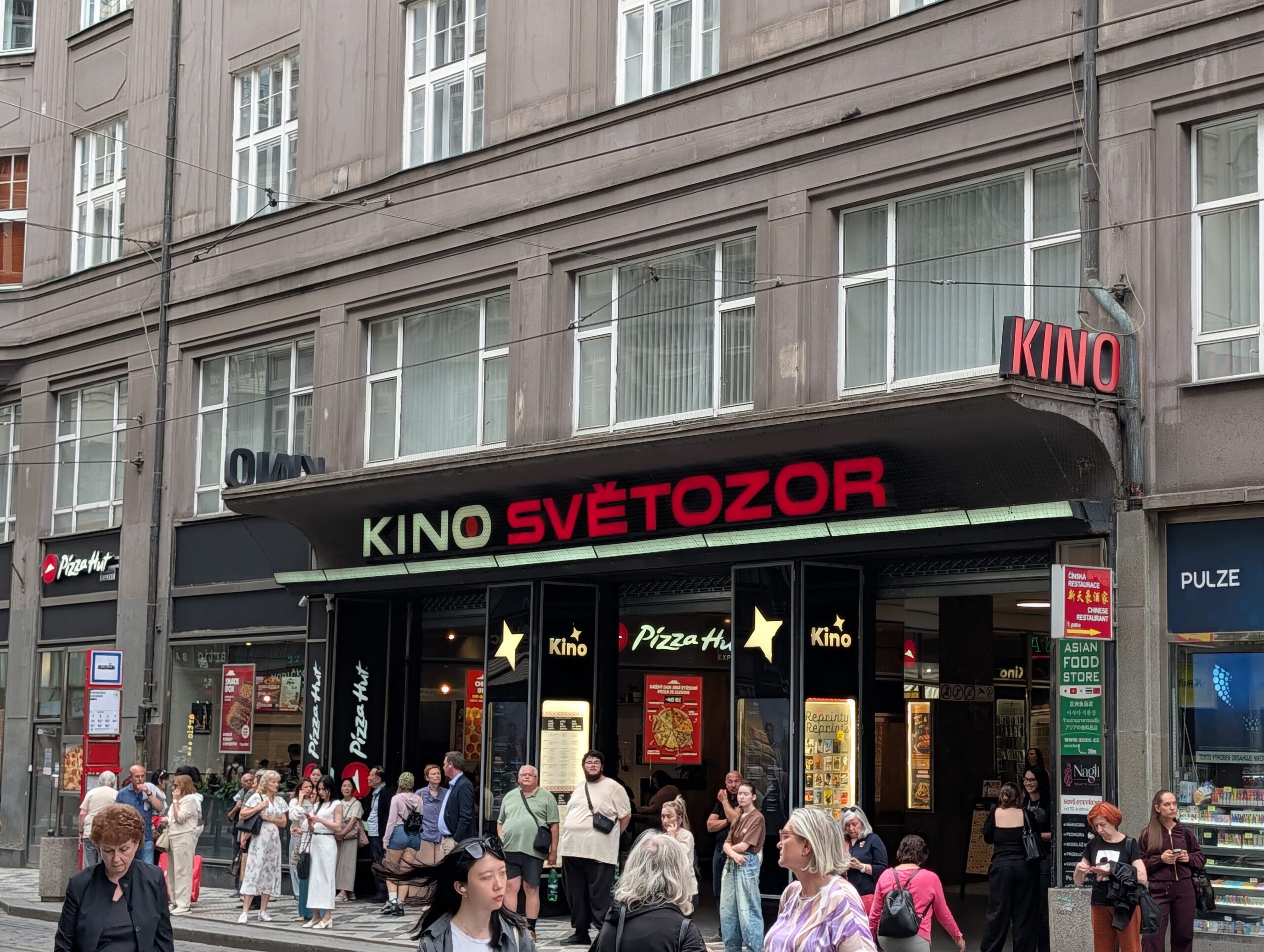 Eingang zum Kino Světozor in Prag mit rot-grünem Schriftzug, wartenden Besuchern und Straßenbahngleisen