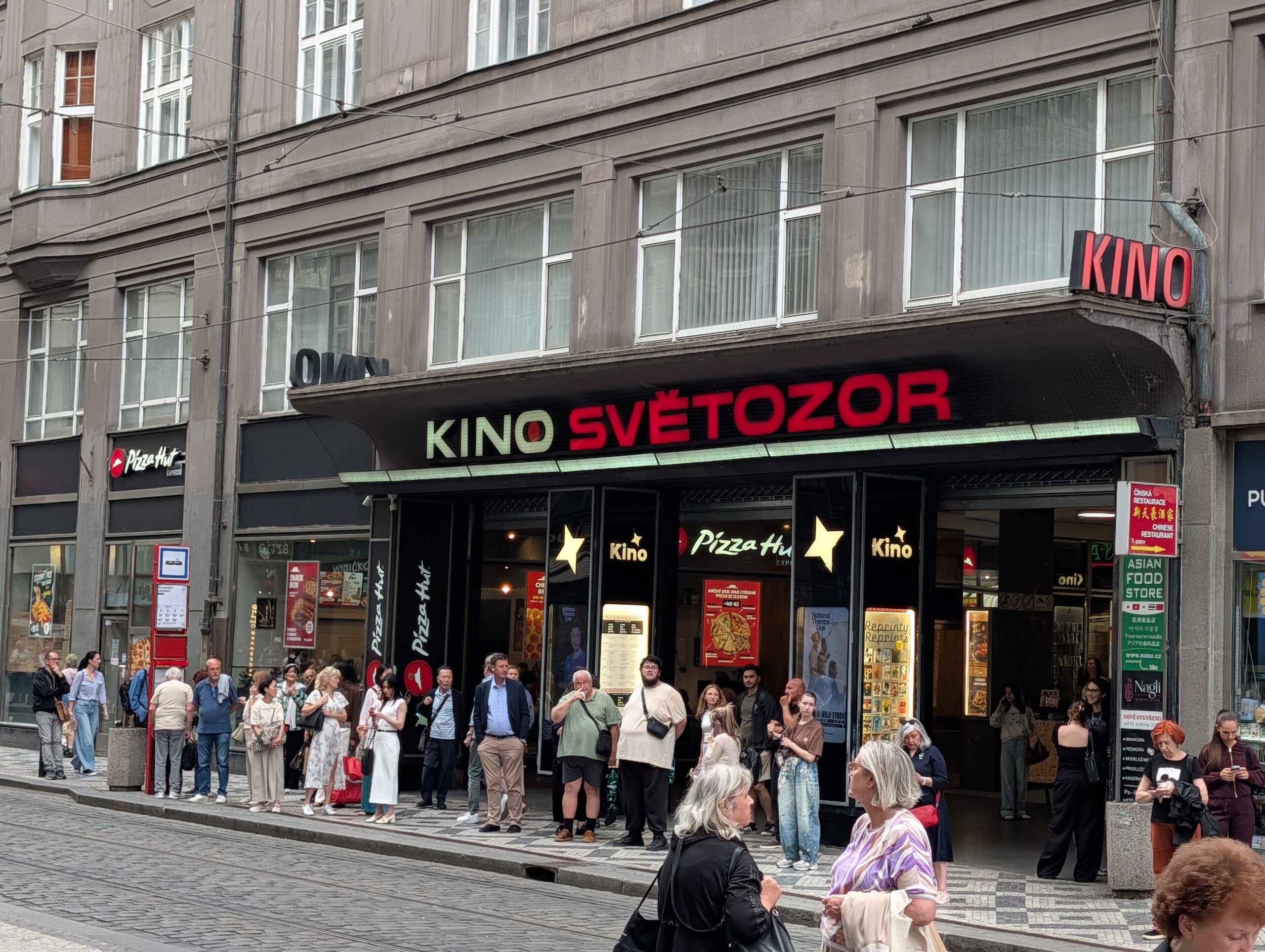 Eingang zum Kino Světozor in Prag mit rot-grünem Schriftzug, wartenden Besuchern und Straßenbahngleisen