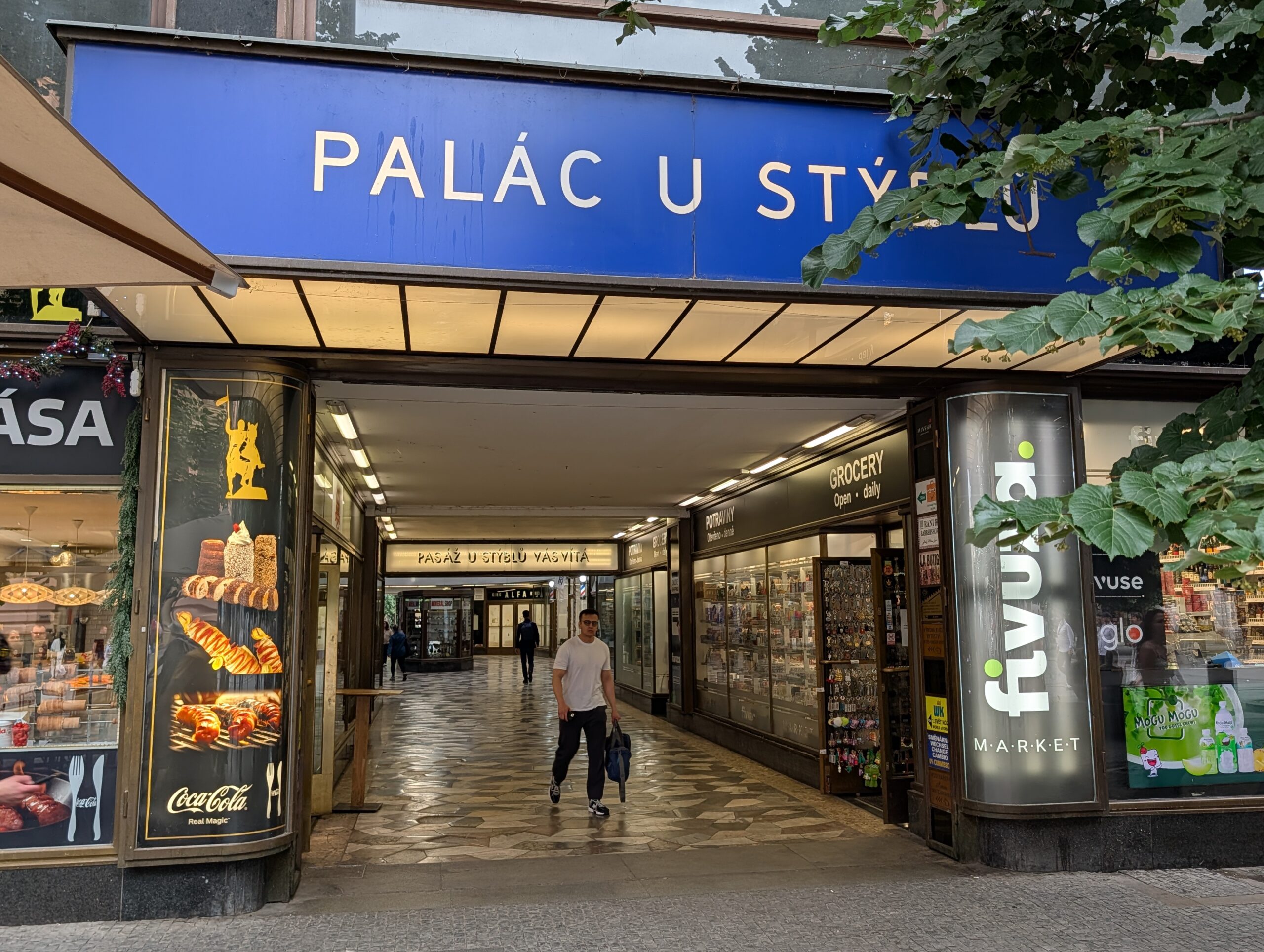 Eingang zum Palast U Stýblů in Prag mit blauem Schriftzug, Passage und angrenzenden Geschäften
