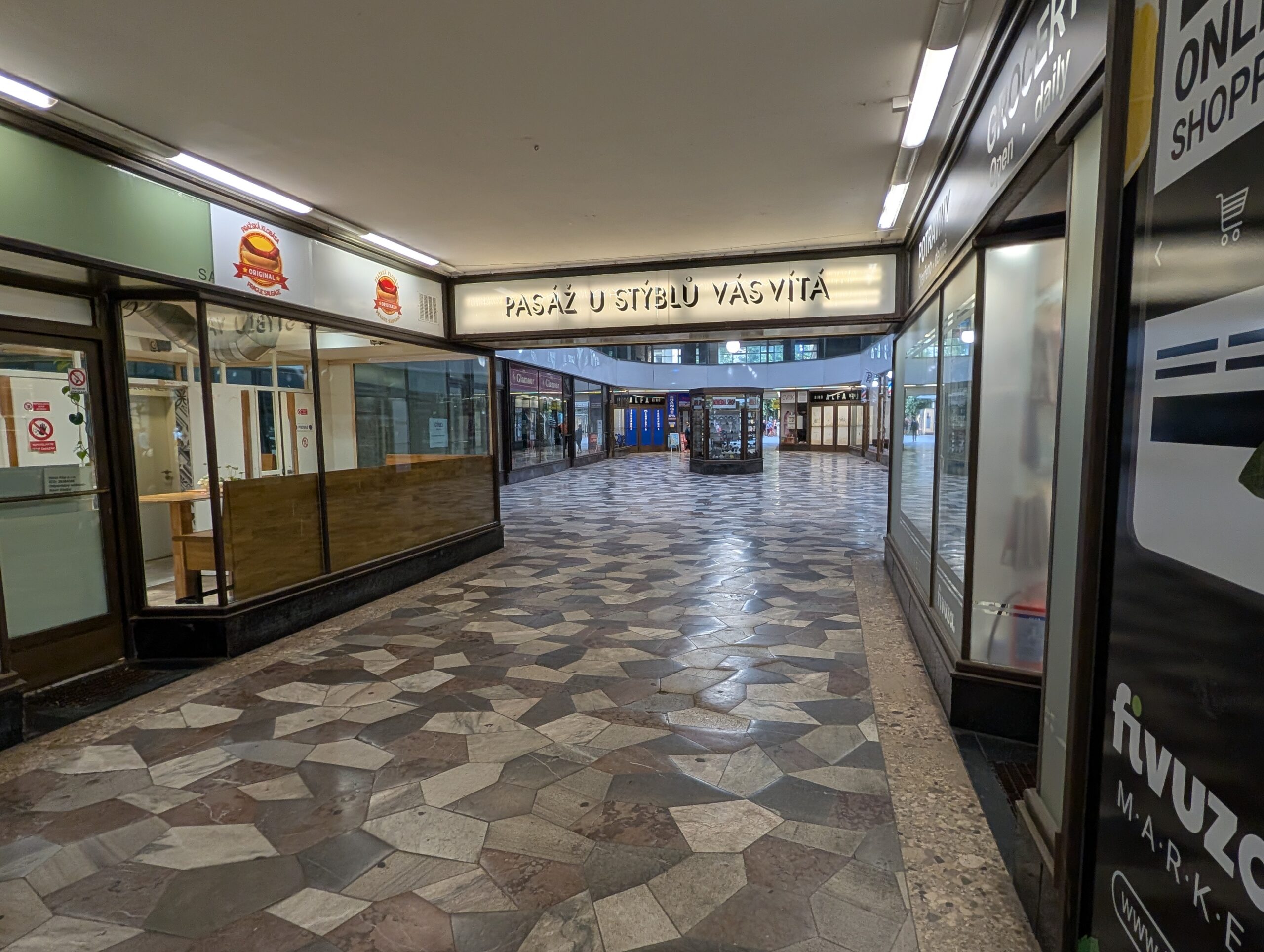 Passage im Palast U Stýblů in Prag mit Geschäften, Steinboden und beleuchtetem Eingangsbereich