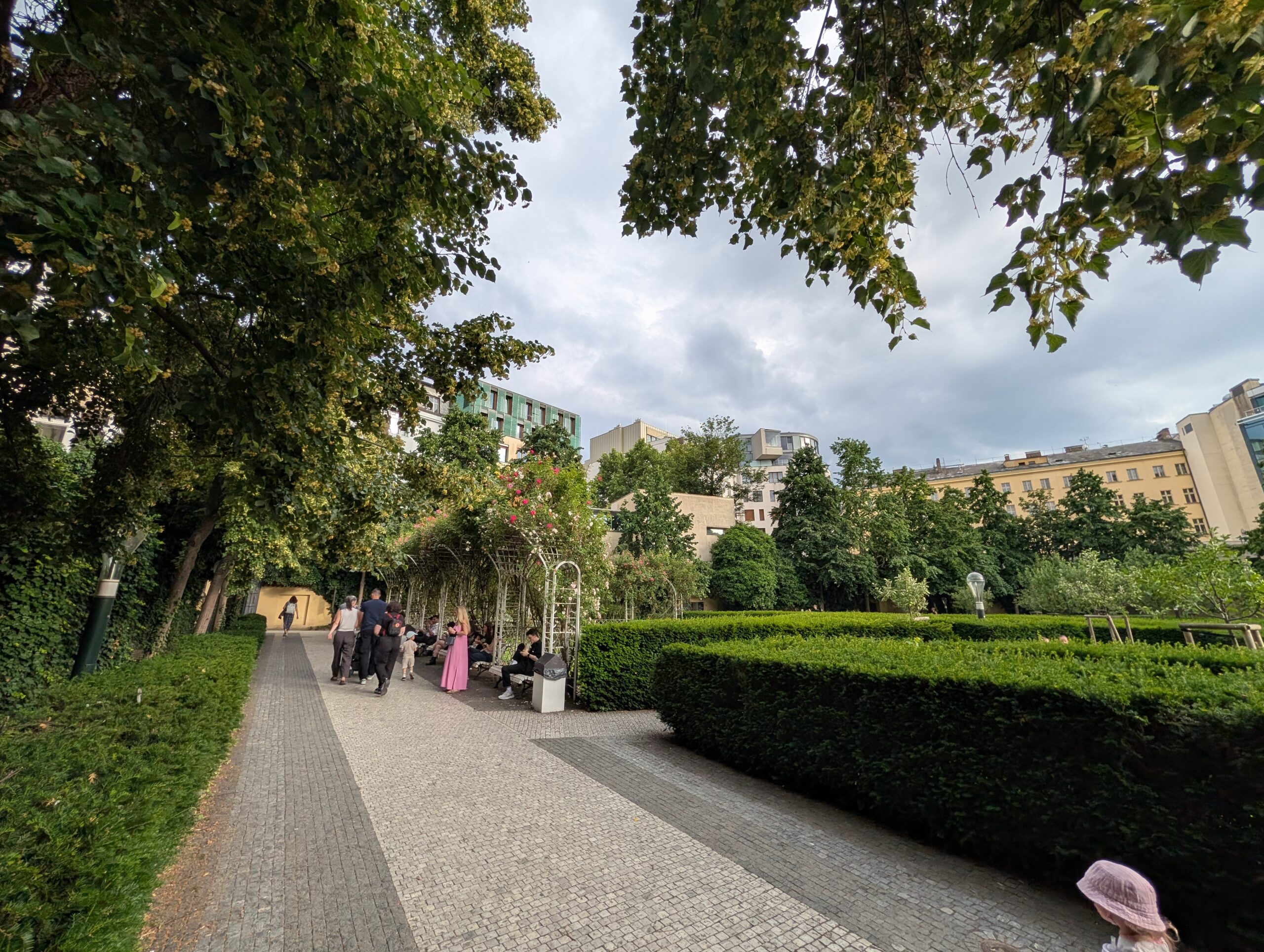 Franziskanergarten in Prag mit Spazierweg, Rosenbögen, geschnittenen Hecken, Bäumen und Besuchern