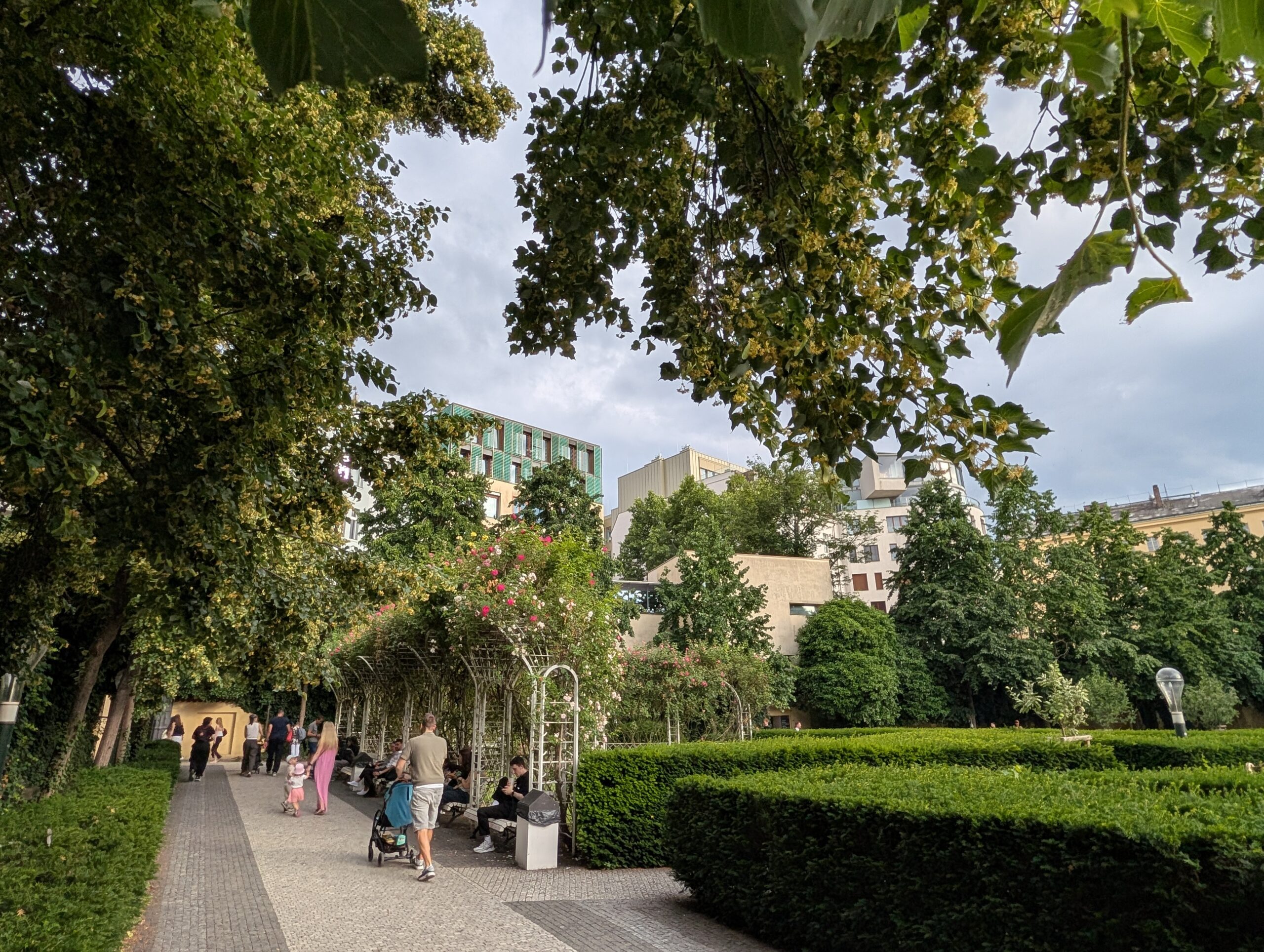 Franziskanergarten in Prag mit Spazierweg, Rosenbögen, geschnittenen Hecken, Bäumen und Besuchern