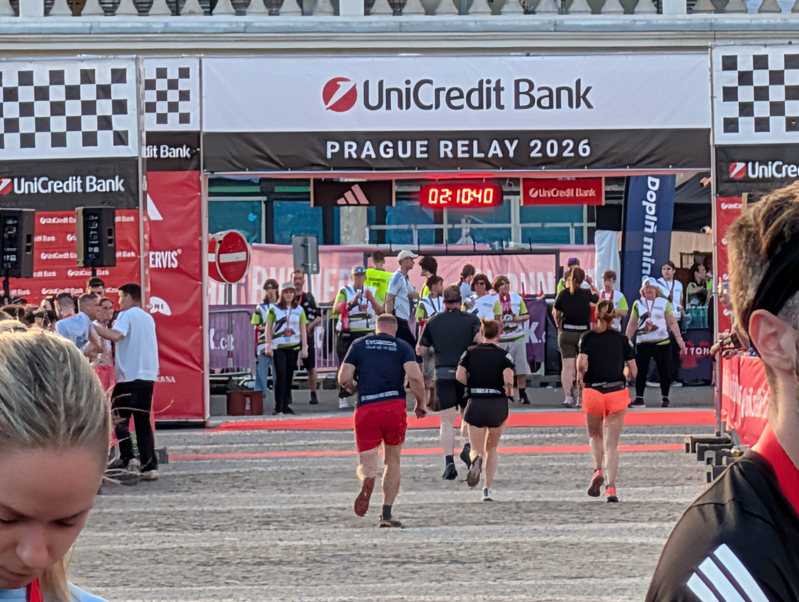 Läufer im Zielbereich des UniCredit Prague Relay 2026 mit Zeitanzeige, Absperrgittern und Veranstaltungsbannern