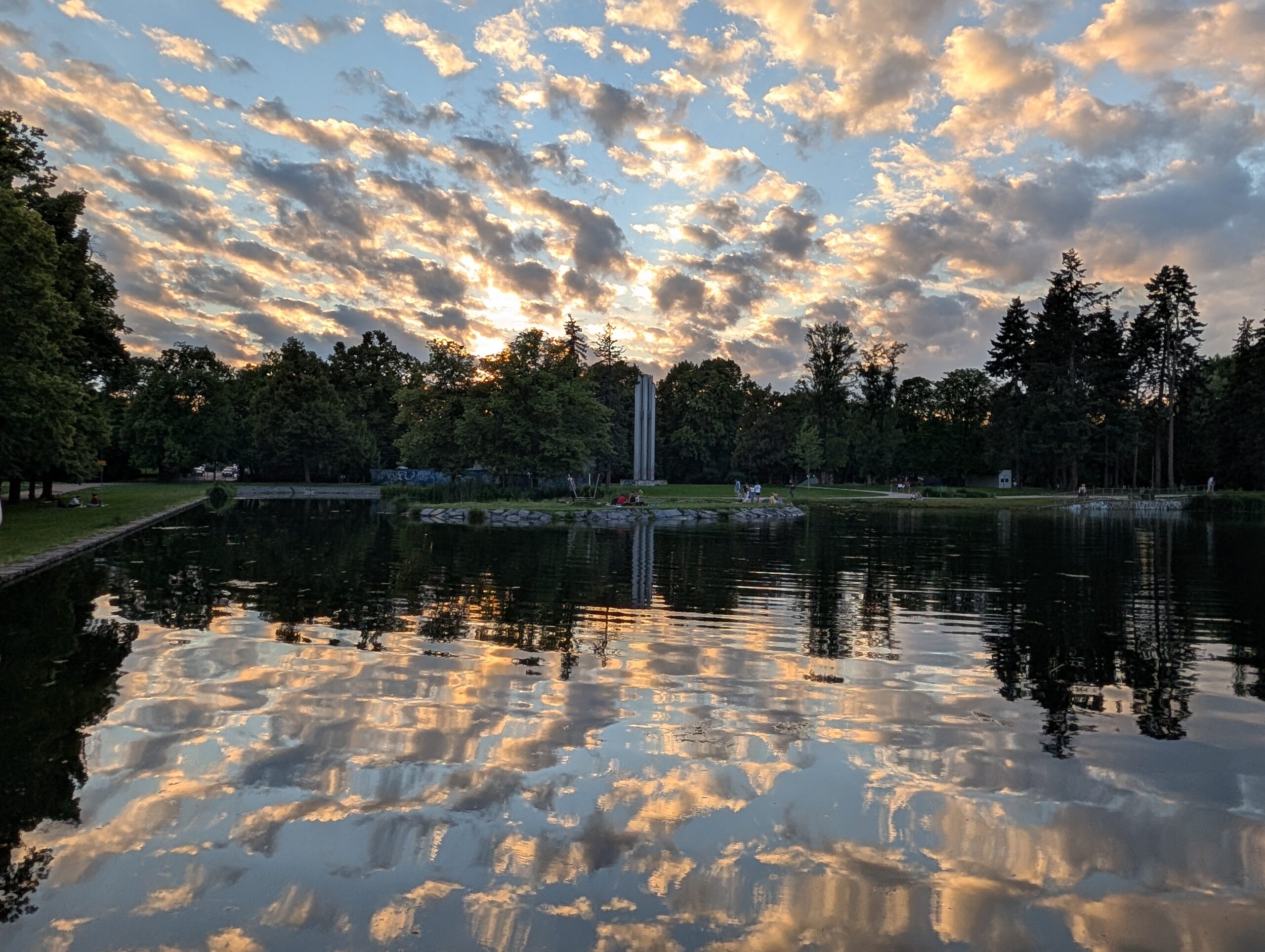 Letná-Teich im Letná-Park bei Sonnenuntergang mit spiegelnden Wolken, Bäumen und Grünflächen