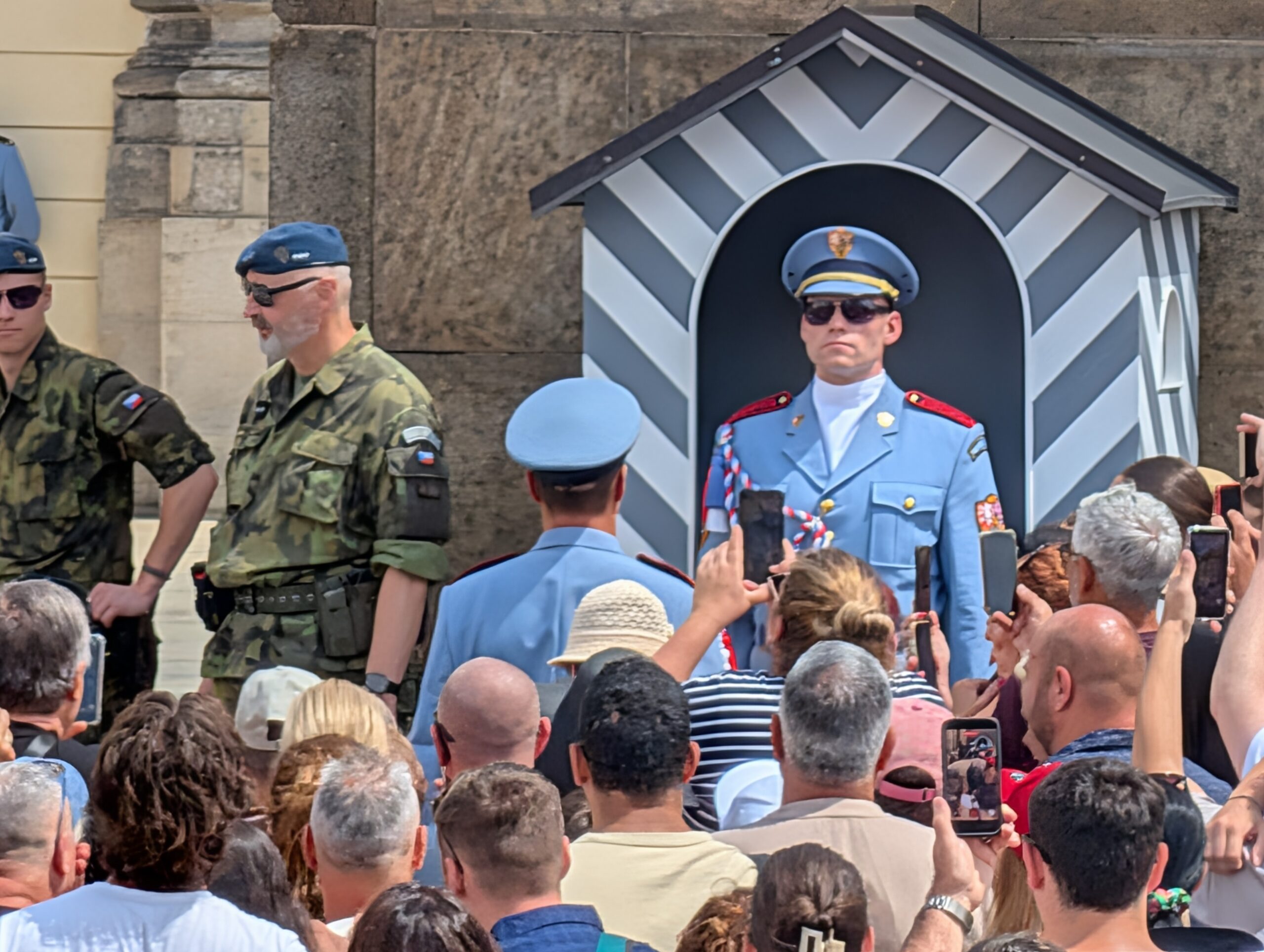 Soldat der Burgwache in hellblauer Uniform vor einem gestreiften Wachhäuschen und zahlreichen Besuchern an der Prager Burg