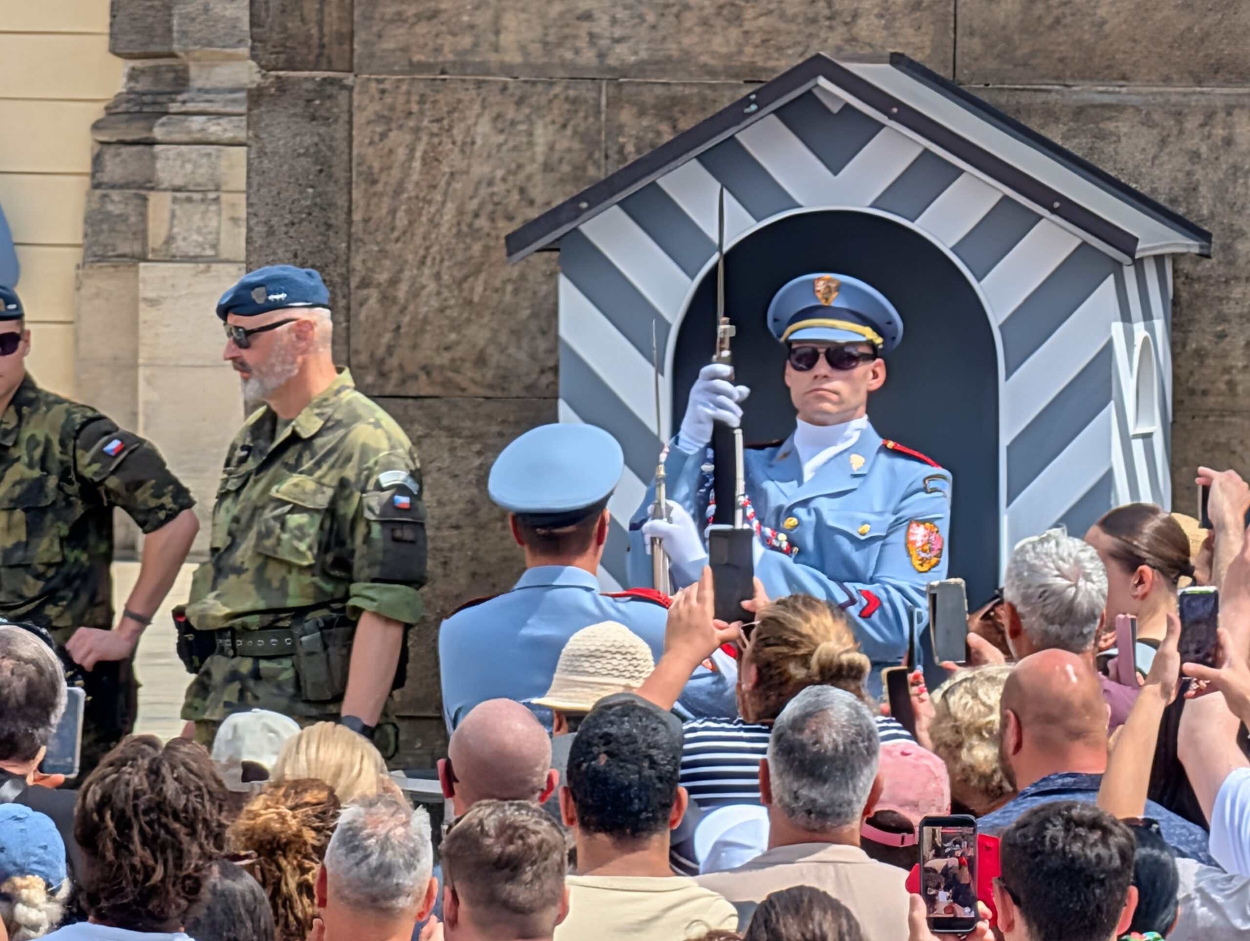 Soldat der Burgwache in hellblauer Uniform vor einem gestreiften Wachhäuschen und zahlreichen Besuchern an der Prager Burg