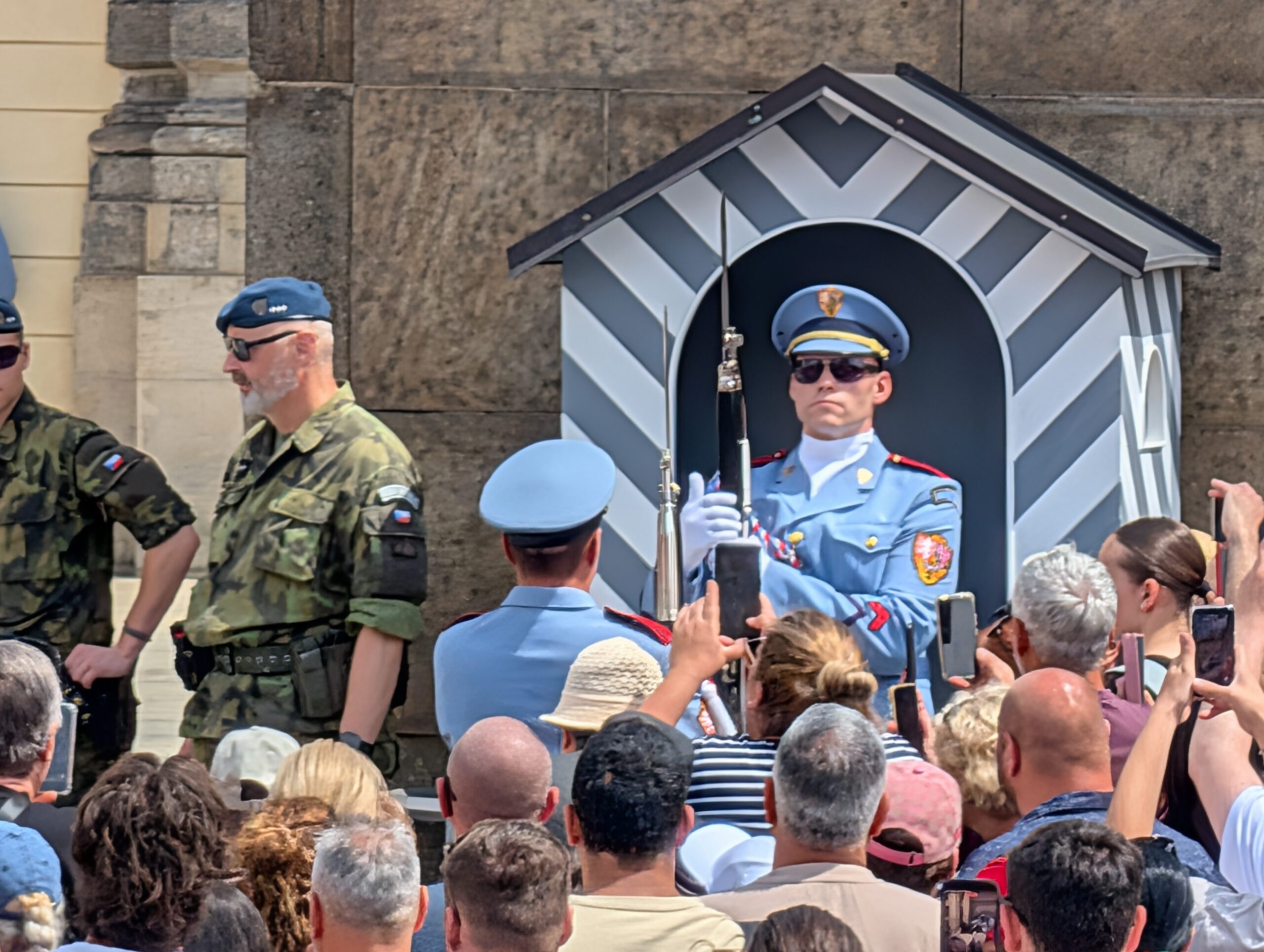 Soldat der Burgwache in hellblauer Uniform vor einem gestreiften Wachhäuschen und zahlreichen Besuchern an der Prager Burg