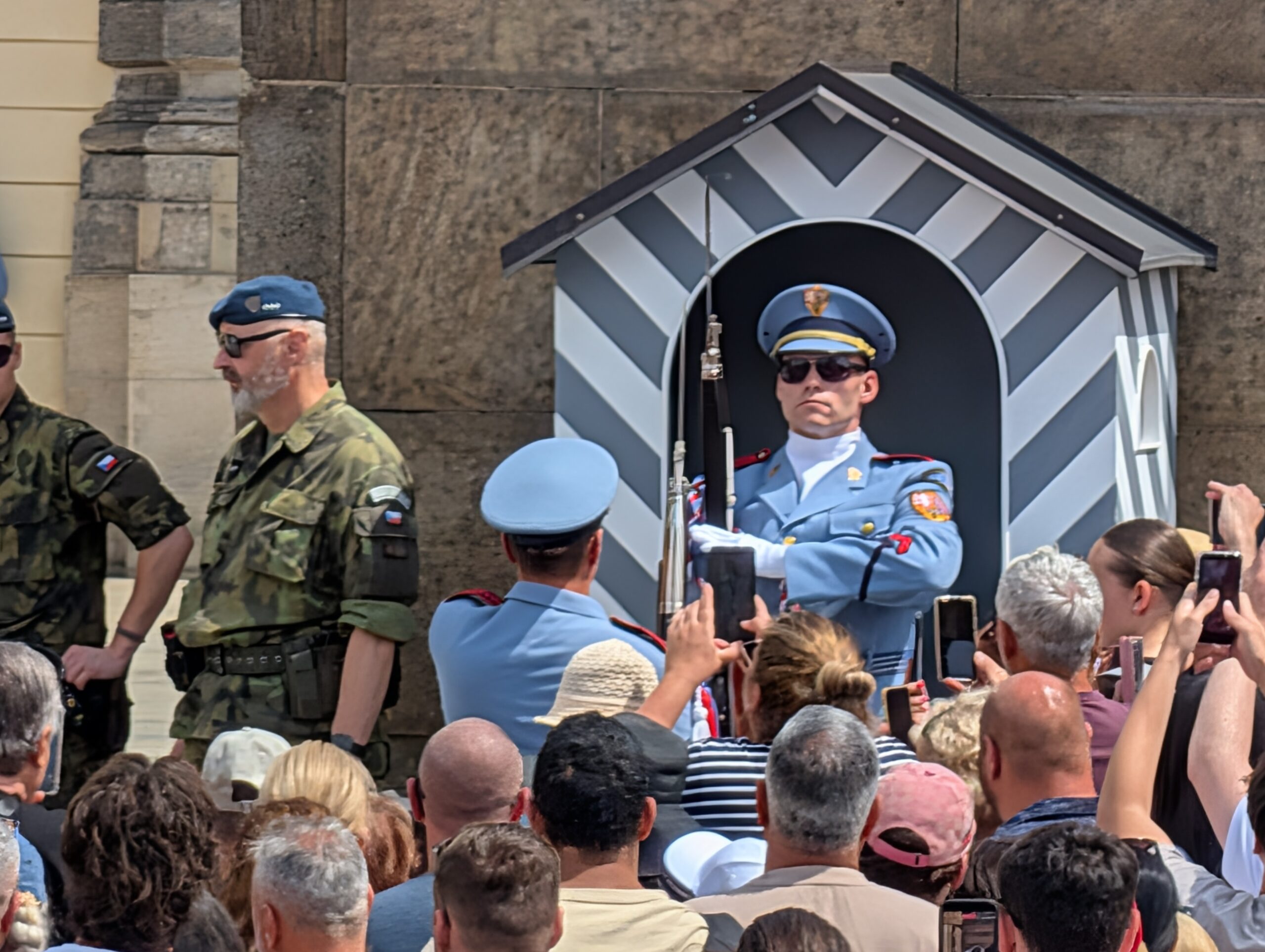Soldat der Burgwache in hellblauer Uniform vor einem gestreiften Wachhäuschen und zahlreichen Besuchern an der Prager Burg