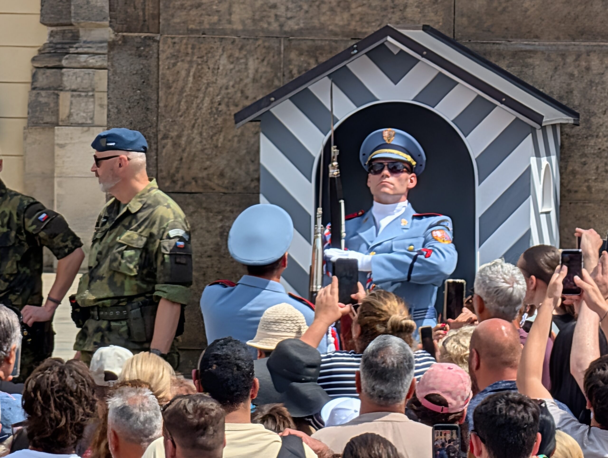 Soldat der Burgwache in hellblauer Uniform vor einem gestreiften Wachhäuschen und zahlreichen Besuchern an der Prager Burg