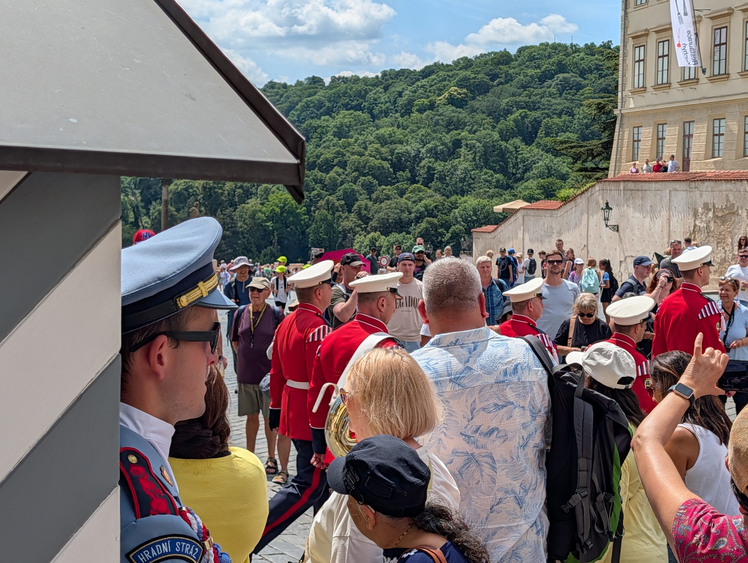 Soldaten der Burgwache und Musiker in roten Uniformen bei der Wachablösung vor Besuchern an der Prager Burg