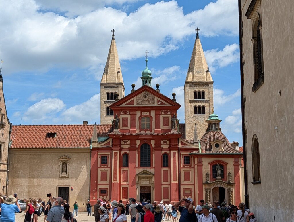 St.-Georgs-Basilika mit roter Barockfassade, zwei romanischen Türmen und Besuchern auf der Prager Burg