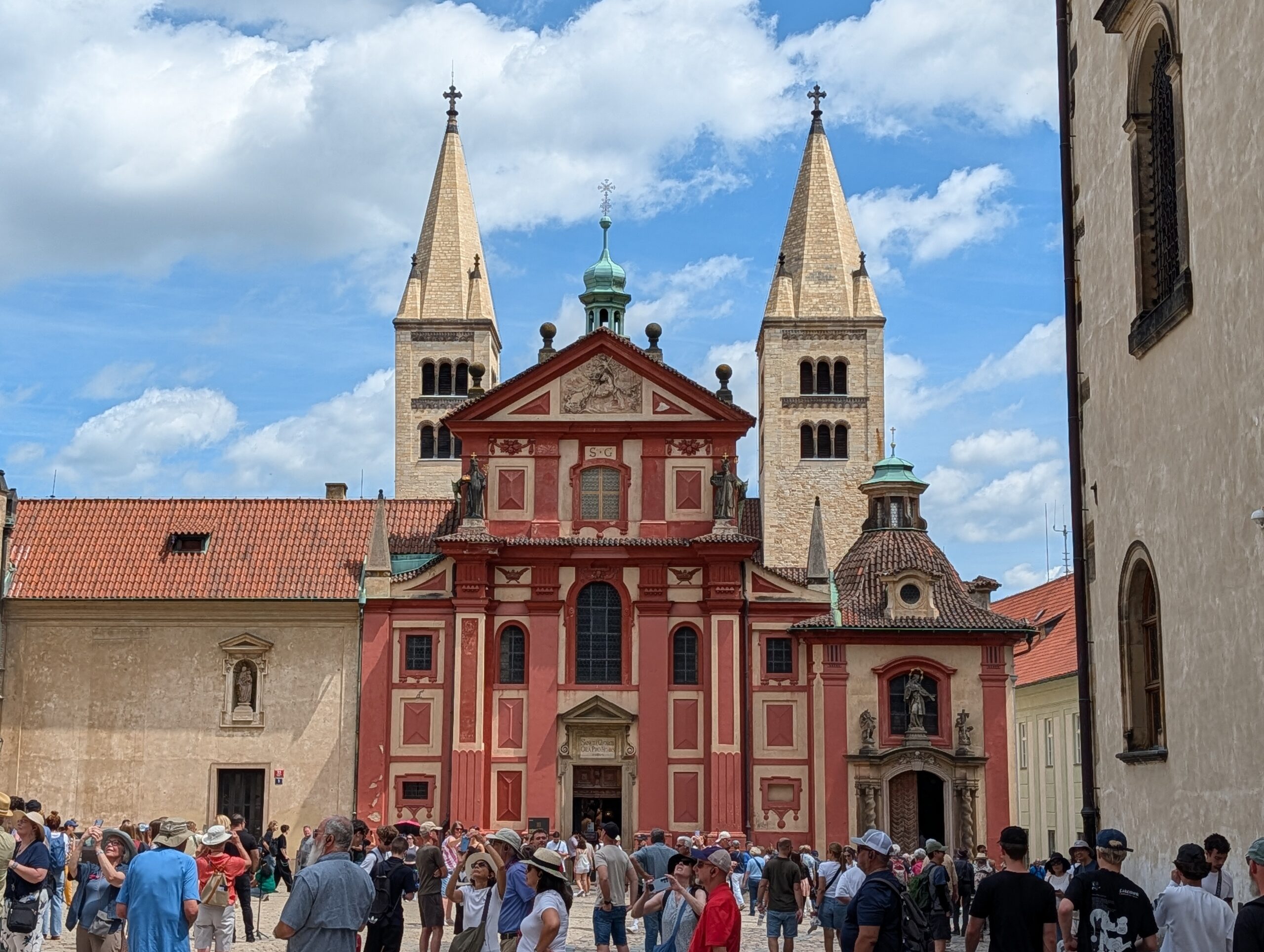 St.-Georgs-Basilika mit roter Barockfassade, zwei romanischen Türmen und Besuchern auf der Prager Burg
