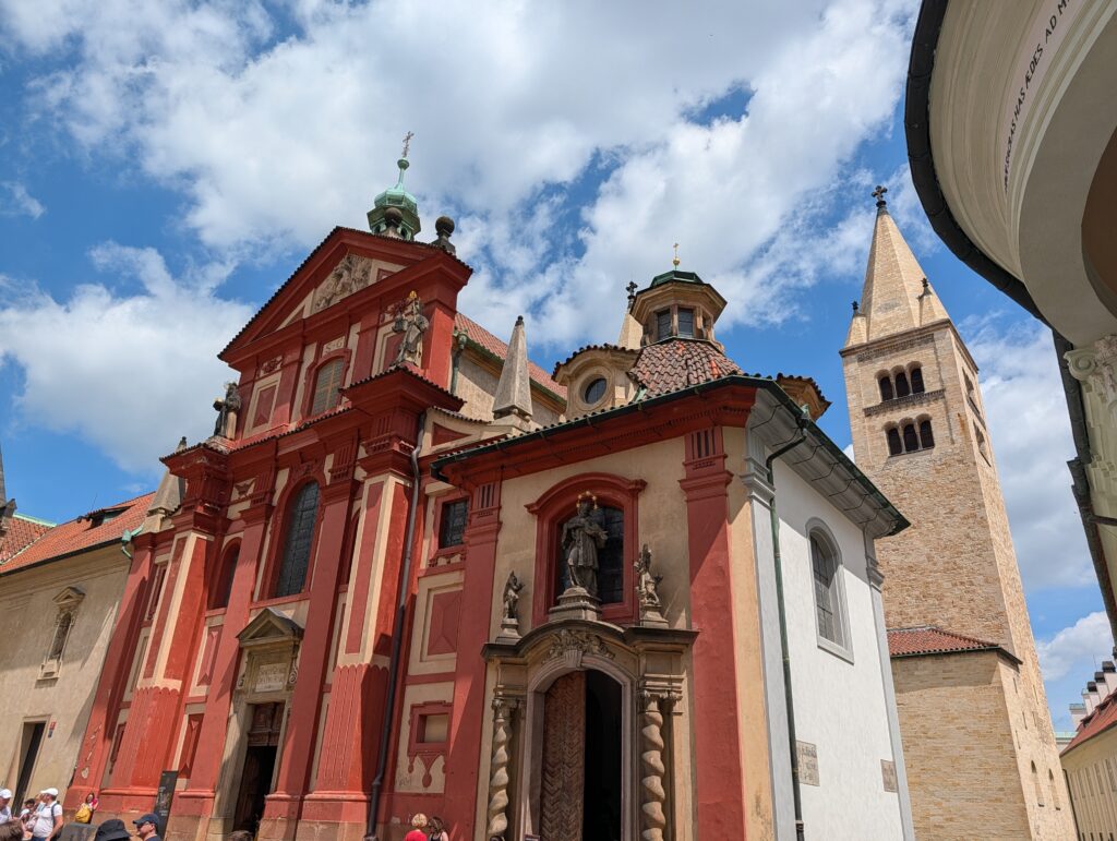 St.-Georgs-Basilika auf der Prager Burg mit roter Barockfassade, Heiligenfiguren und romanischen Türmen