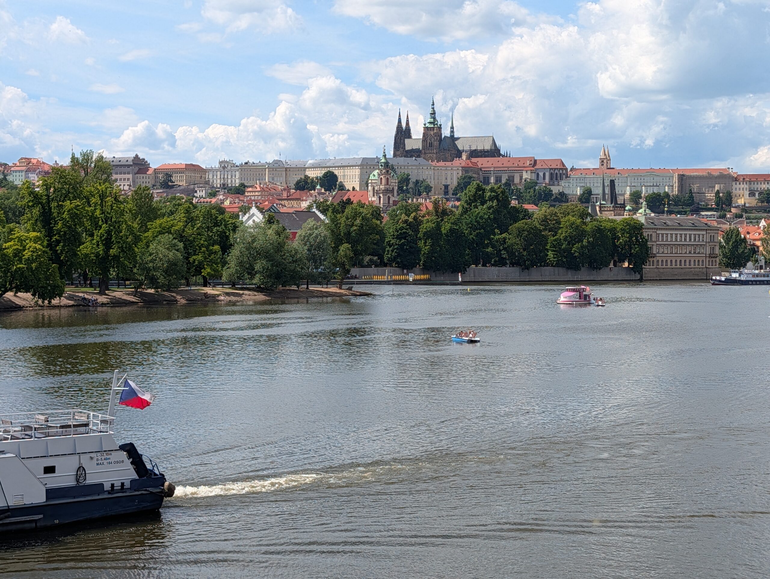 Blick über die Moldau auf Prager Burg und Veitsdom mit Ausflugsschiff und kleinen Booten