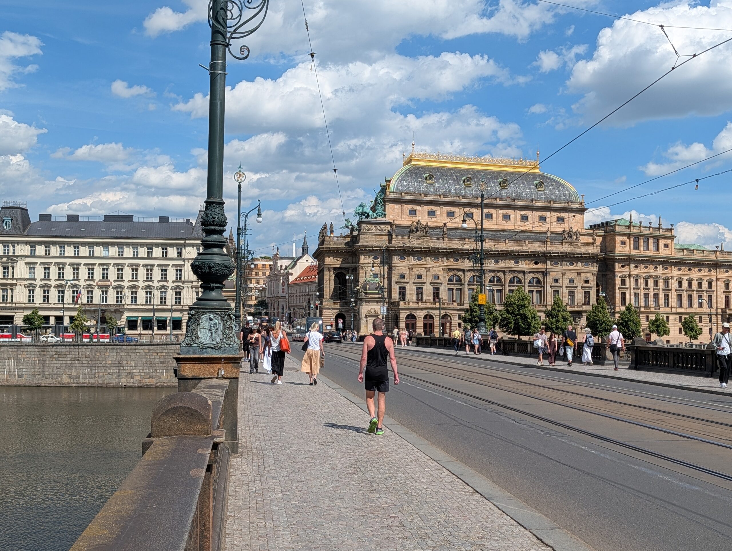 Brücke der Legionen in Prag mit Gehweg, Straßenbahngleisen, Passanten und Nationaltheater im Hintergrund