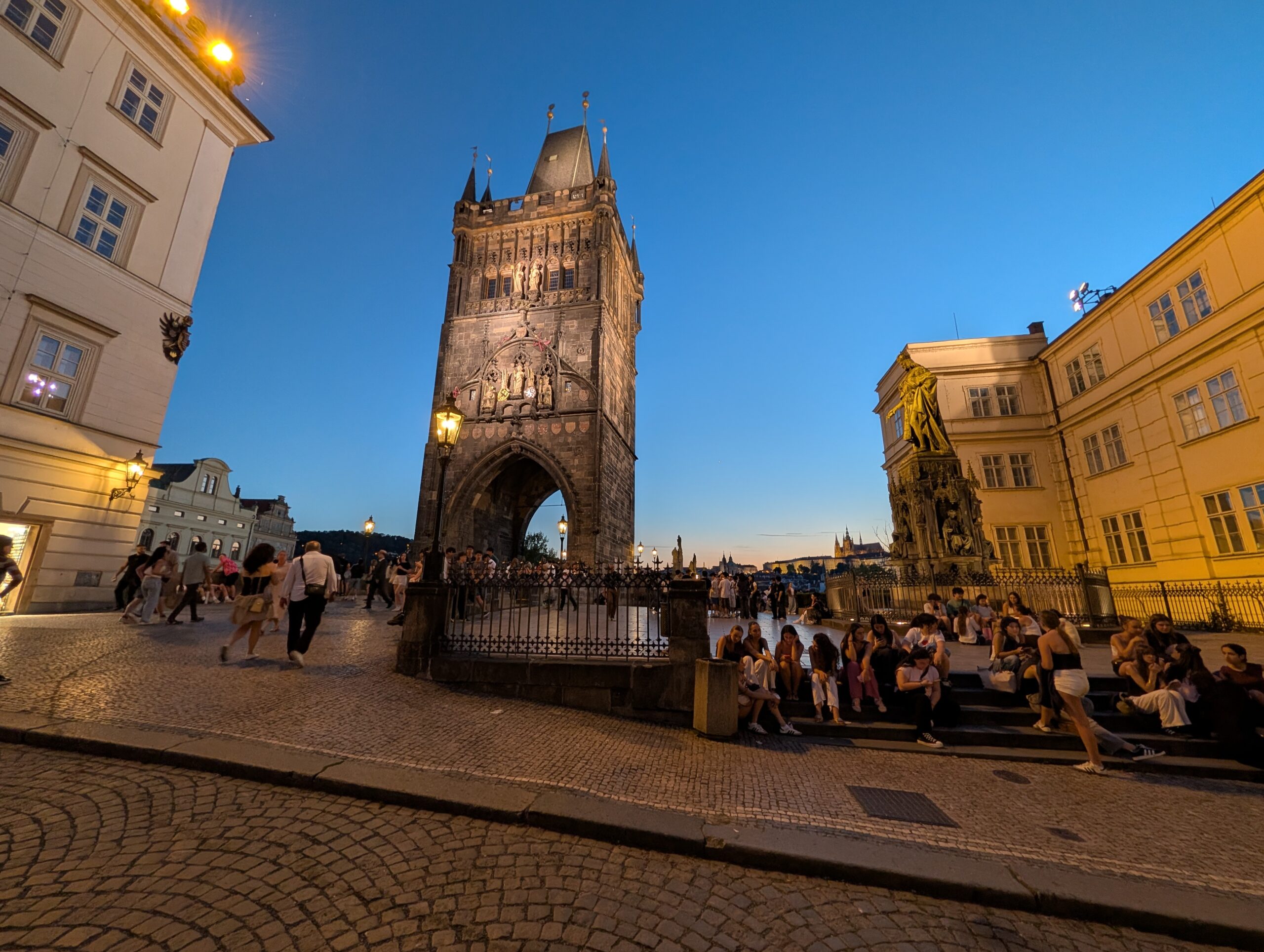 Altstädter Brückenturm am belebten Kreuzherrenplatz mit Karls-IV.-Denkmal bei Abenddämmerung
