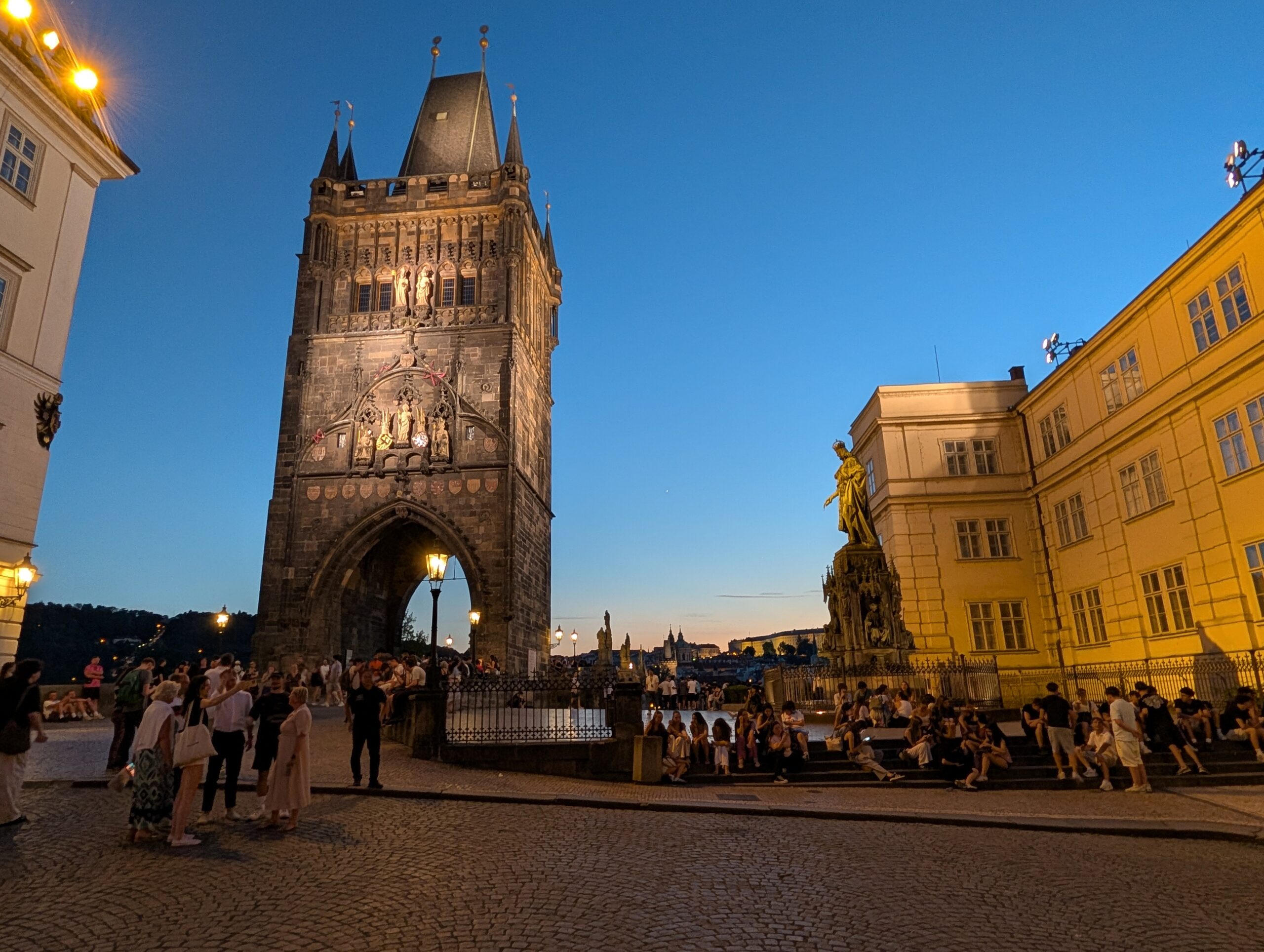 Altstädter Brückenturm am belebten Kreuzherrenplatz mit Karls-IV.-Denkmal bei Abenddämmerung