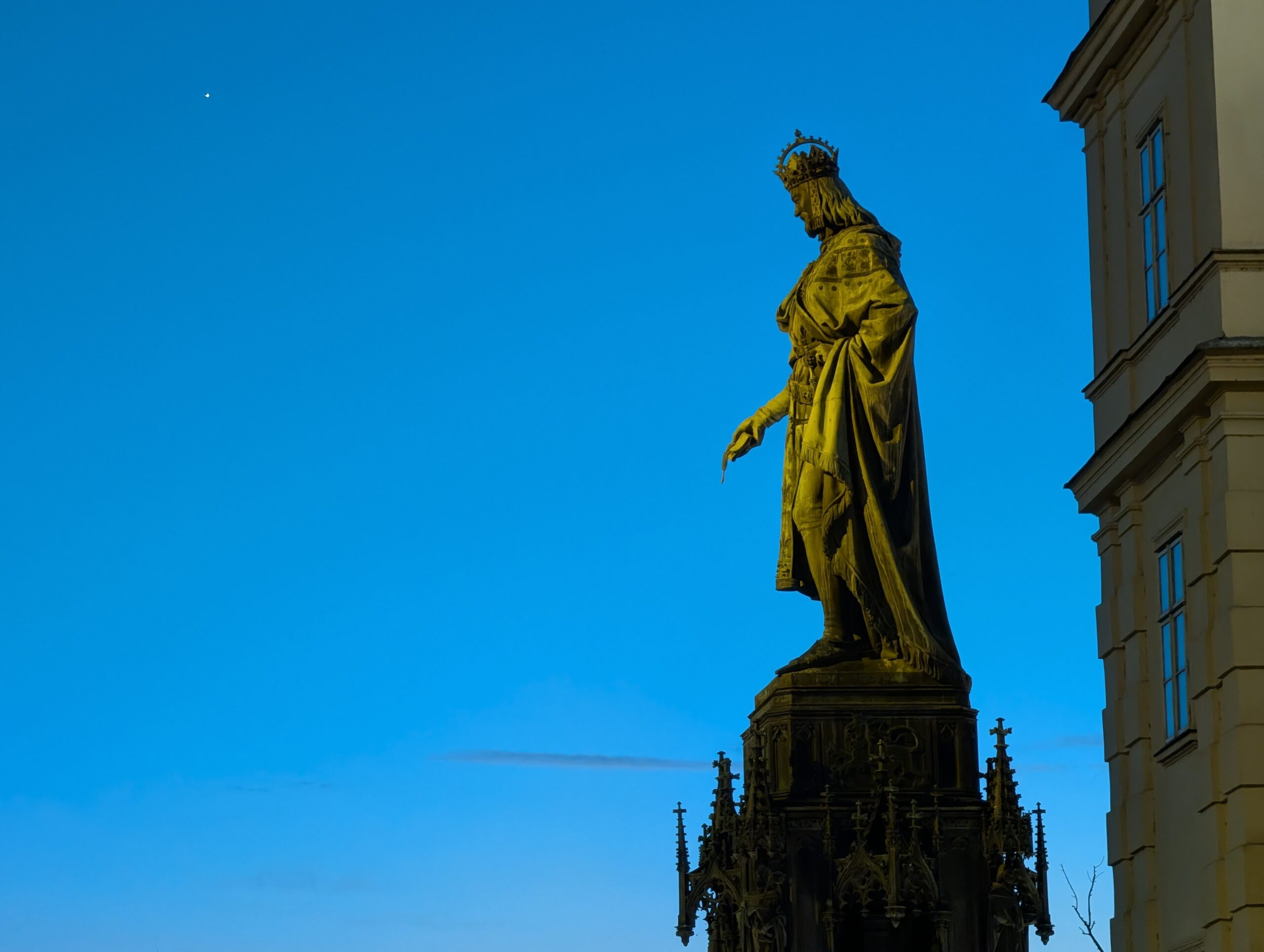Beleuchtete Statue von Karl IV. auf reich verziertem Sockel am Kreuzherrenplatz bei Abenddämmerung