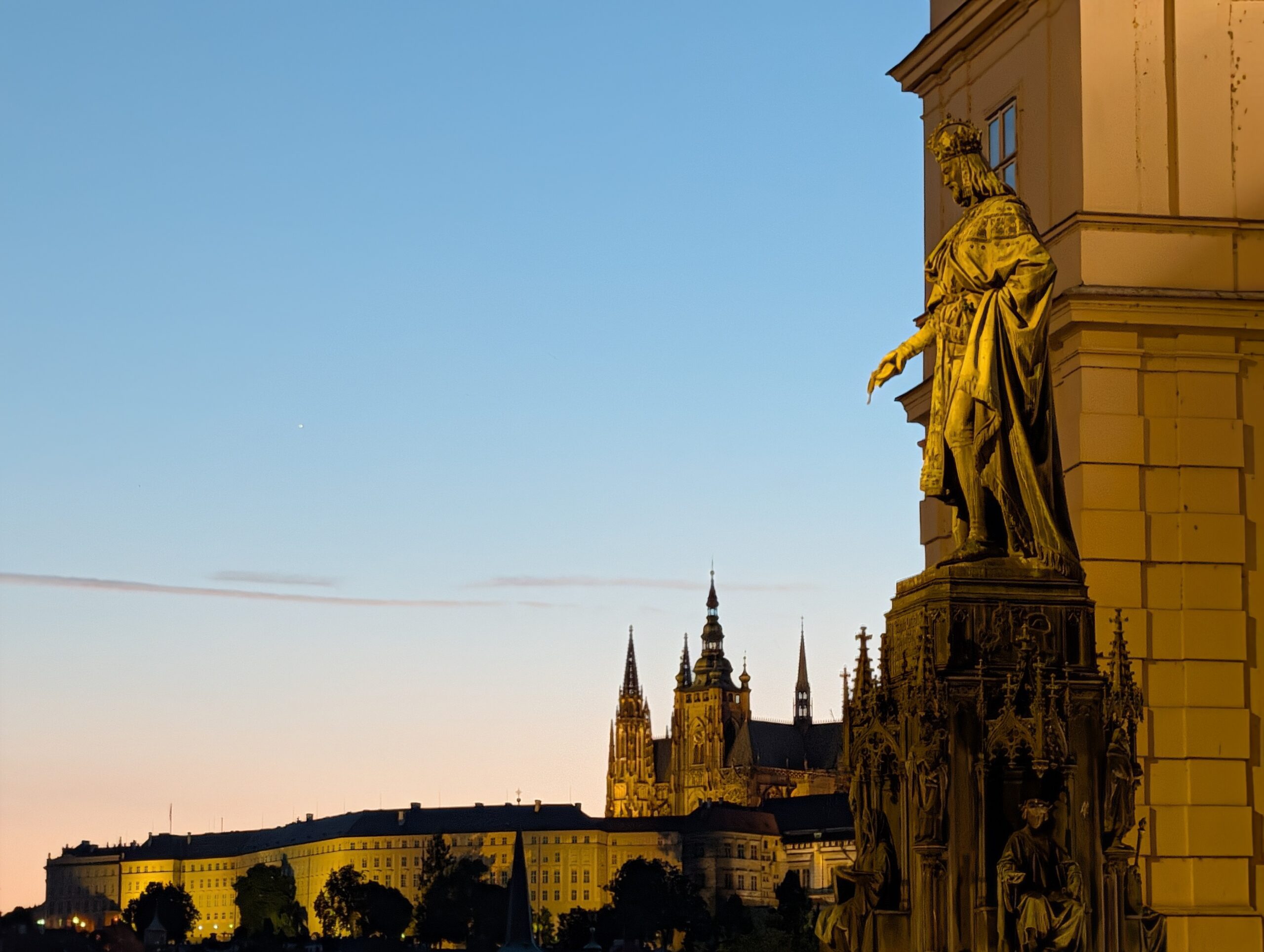 Karl IV.-Denkmal am Kreuzherrenplatz mit beleuchteter Prager Burg und Veitsdom bei Abenddämmerung