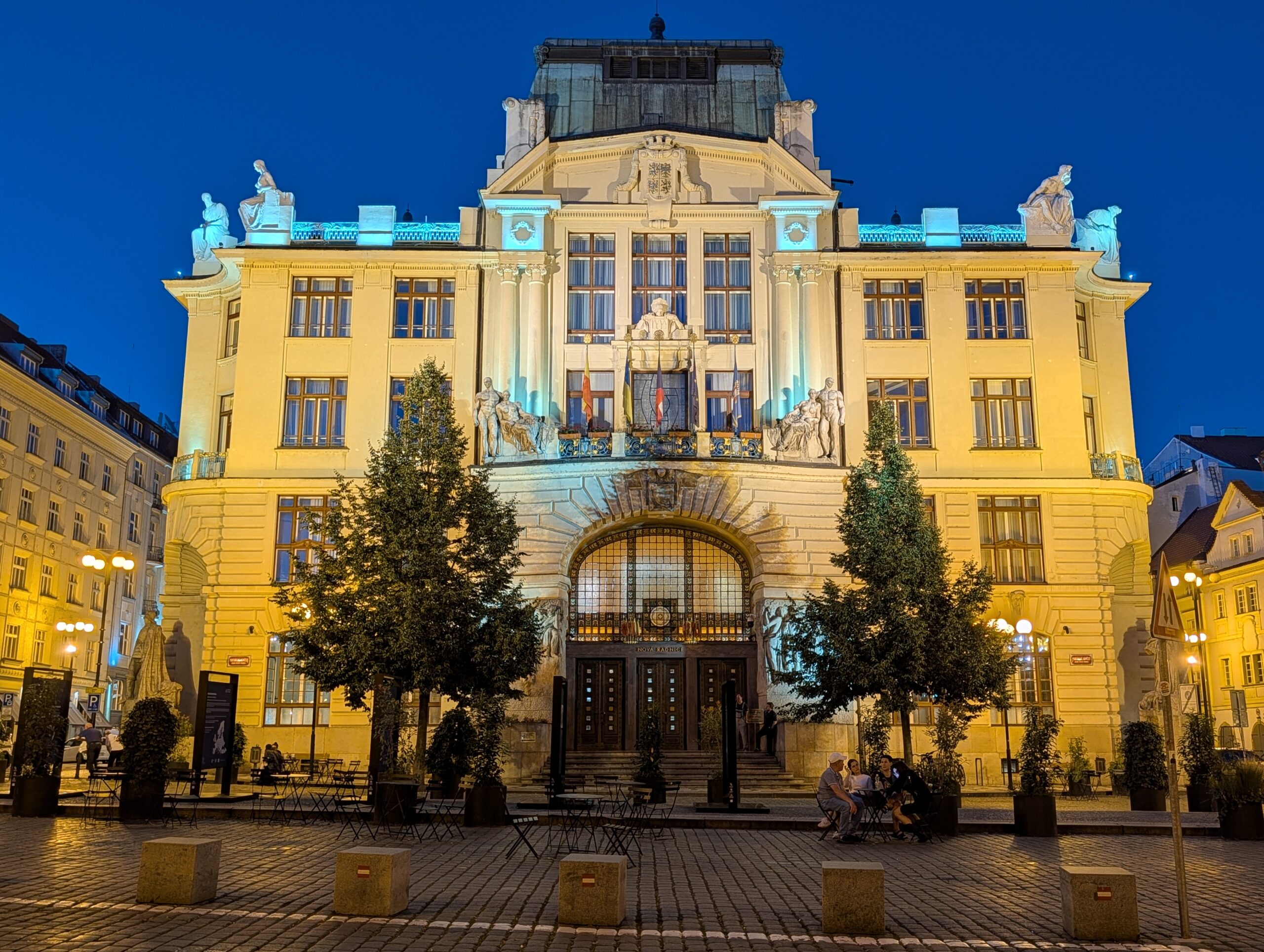 Beleuchtetes Neues Rathaus mit Skulpturen und Rundbogenportal am Marienplatz in Prag bei Nacht