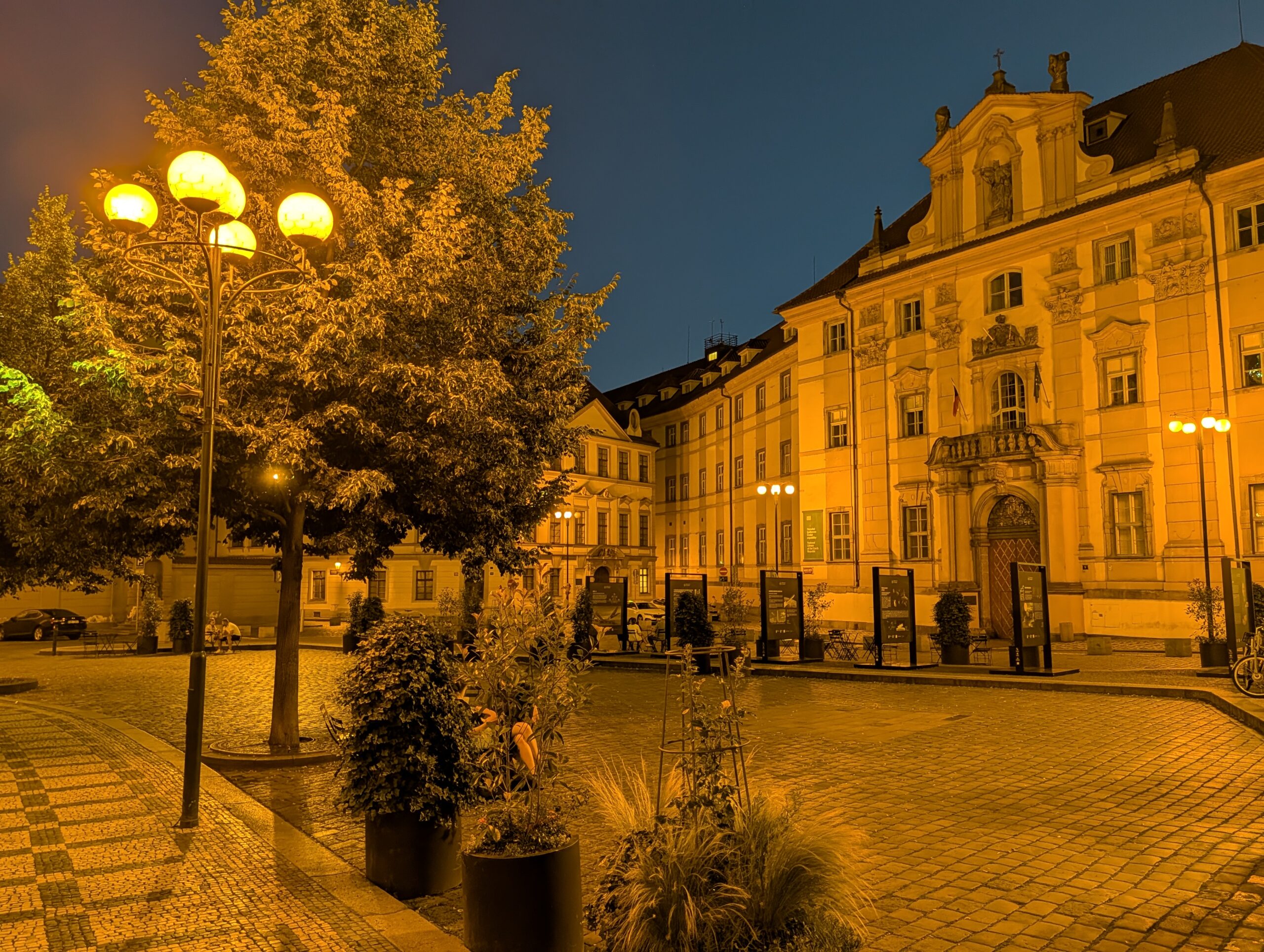 Marienplatz in Prag bei Nacht mit historischen Gebäuden, Straßenlaternen, Bäumen und Eingang zum Klementinum