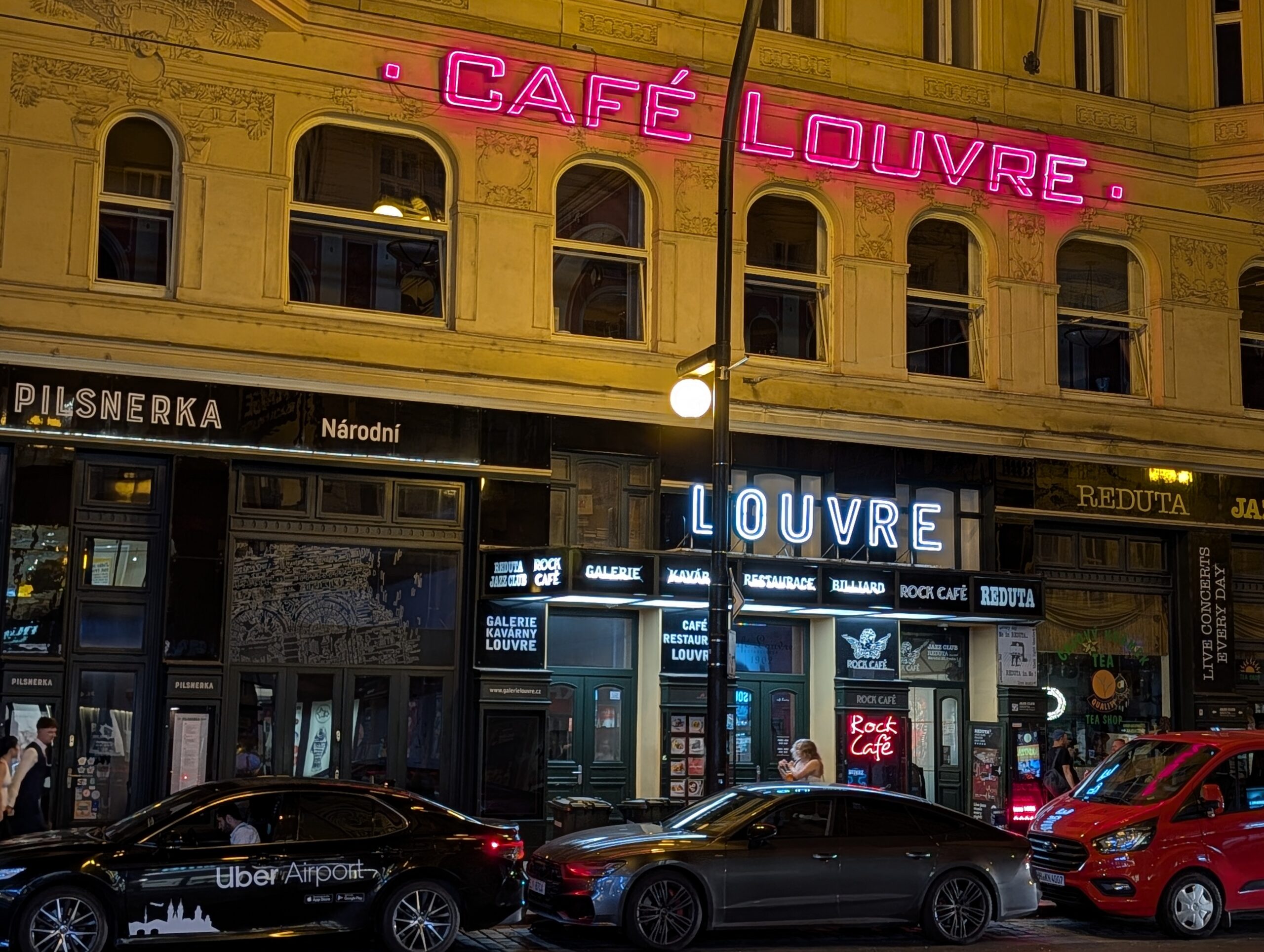 Beleuchtete Fassade des historischen Café Louvre mit auffälliger Neonreklame an der Národní třída bei Nacht in Prag.