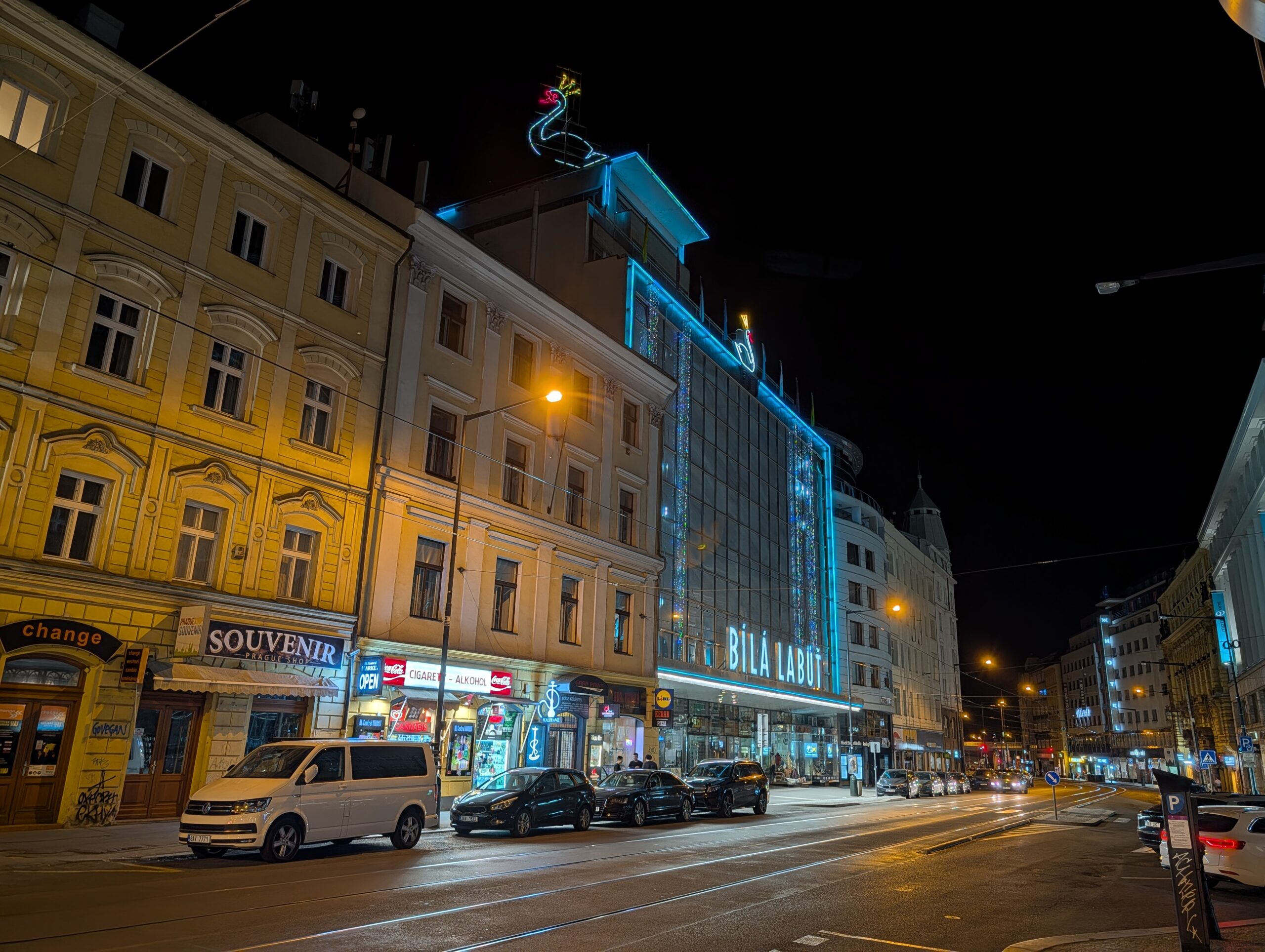 Nächtliches Straßenbild mit dem beleuchteten Kaufhaus Bílá labuť und historischen Gebäuden im Zentrum von Prag.
