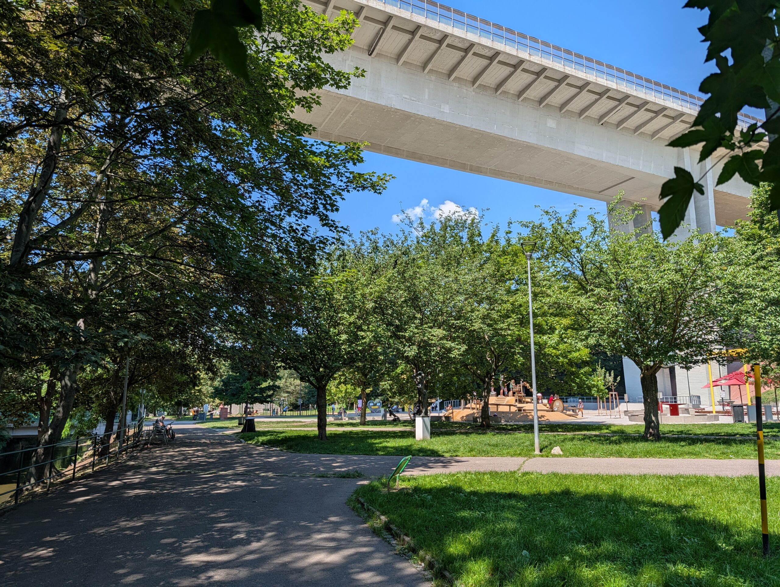 Spazierweg und Grünflächen im Park Folimanka unter der Nusle-Brücke in Prag an einem sonnigen Sommertag.