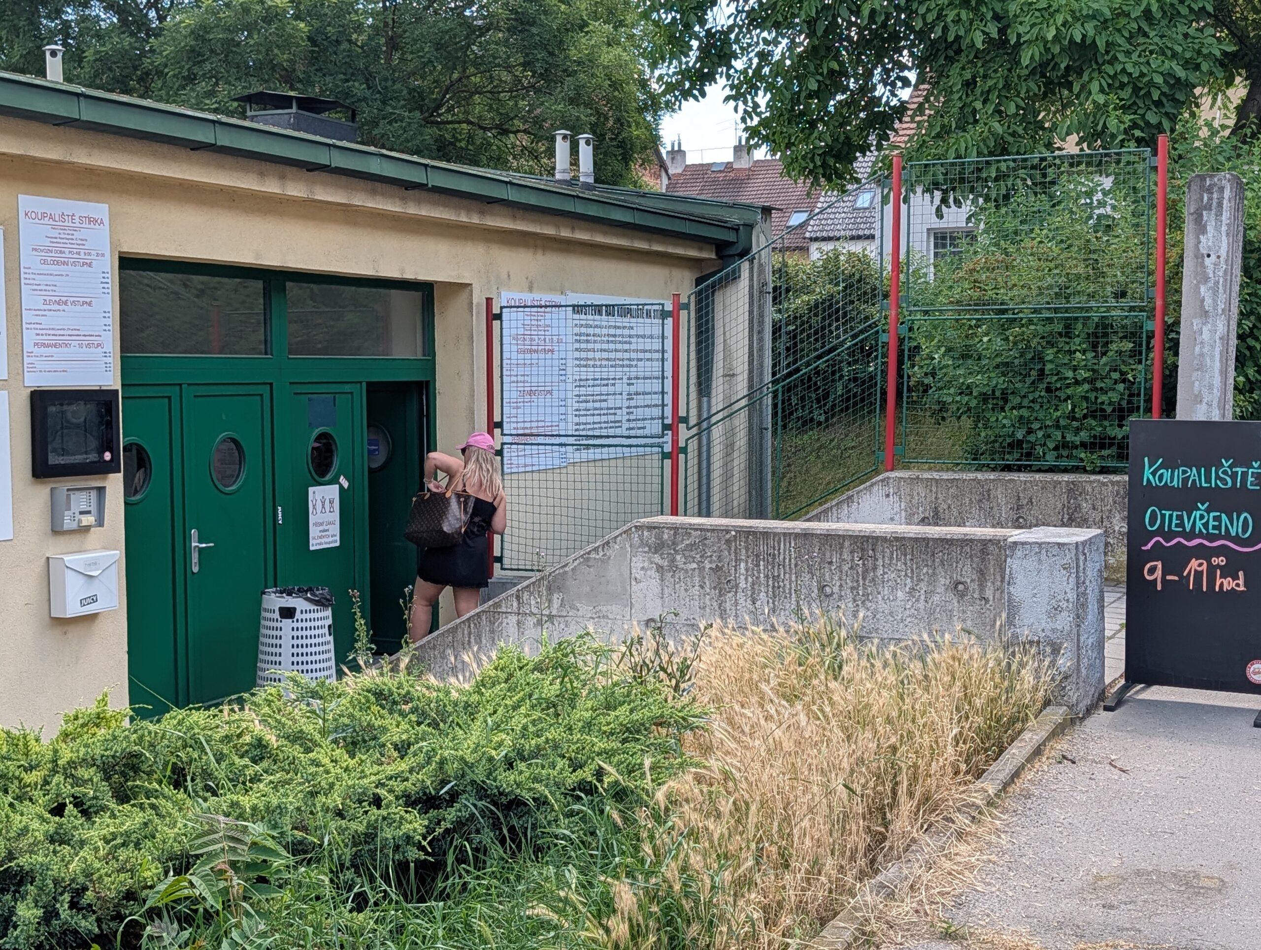 Eingang des Freibads Stírka (Koupaliště Stírka) in Prag mit Kassenbereich, Informationstafel und Hinweisschild zu den Öffnungszeiten.