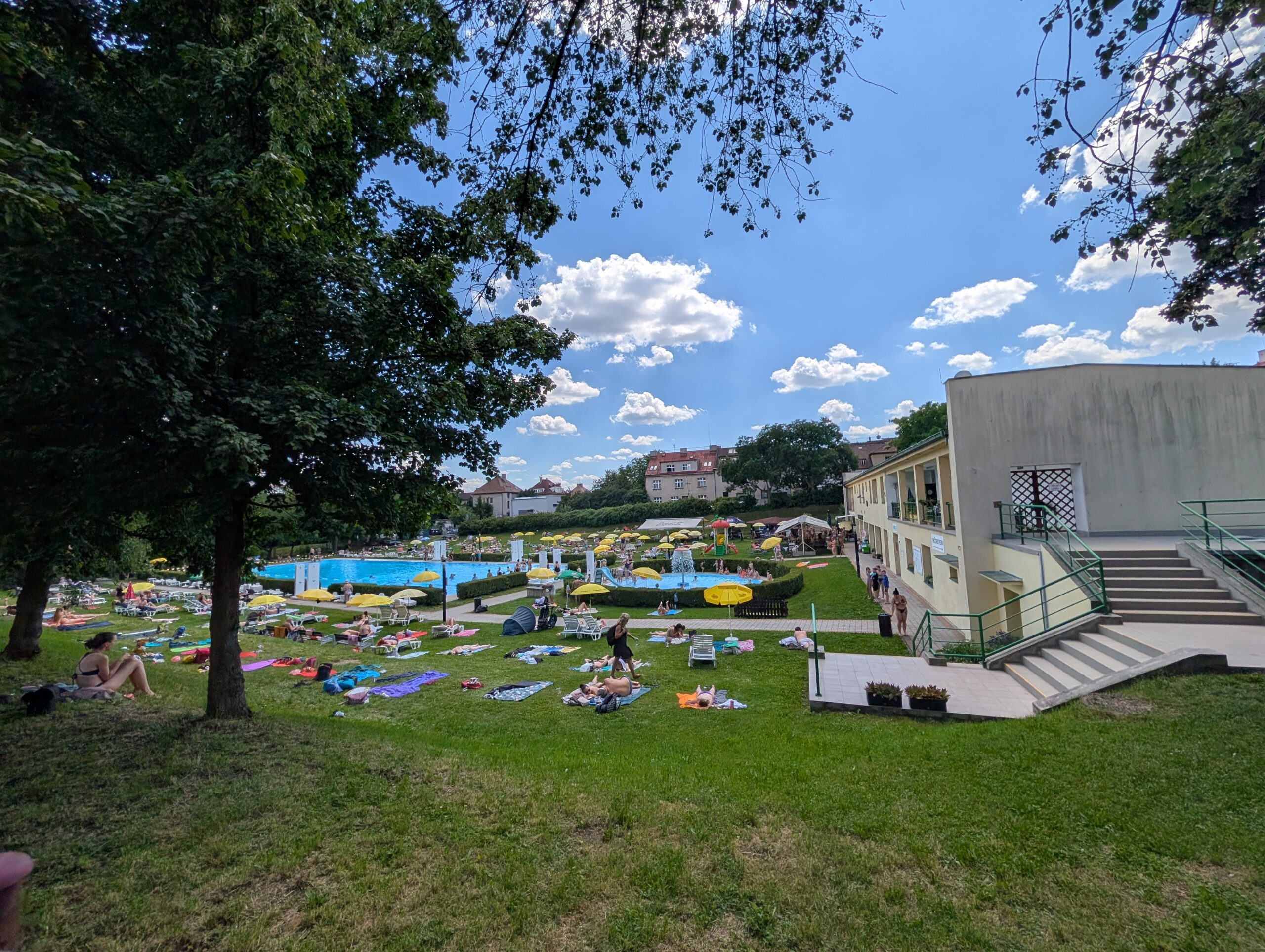 Liegewiese und Schwimmbecken des Freibads Stírka (Koupaliště Stírka) im Prager Stadtteil Kobylisy mit Badegästen an einem sonnigen Tag.