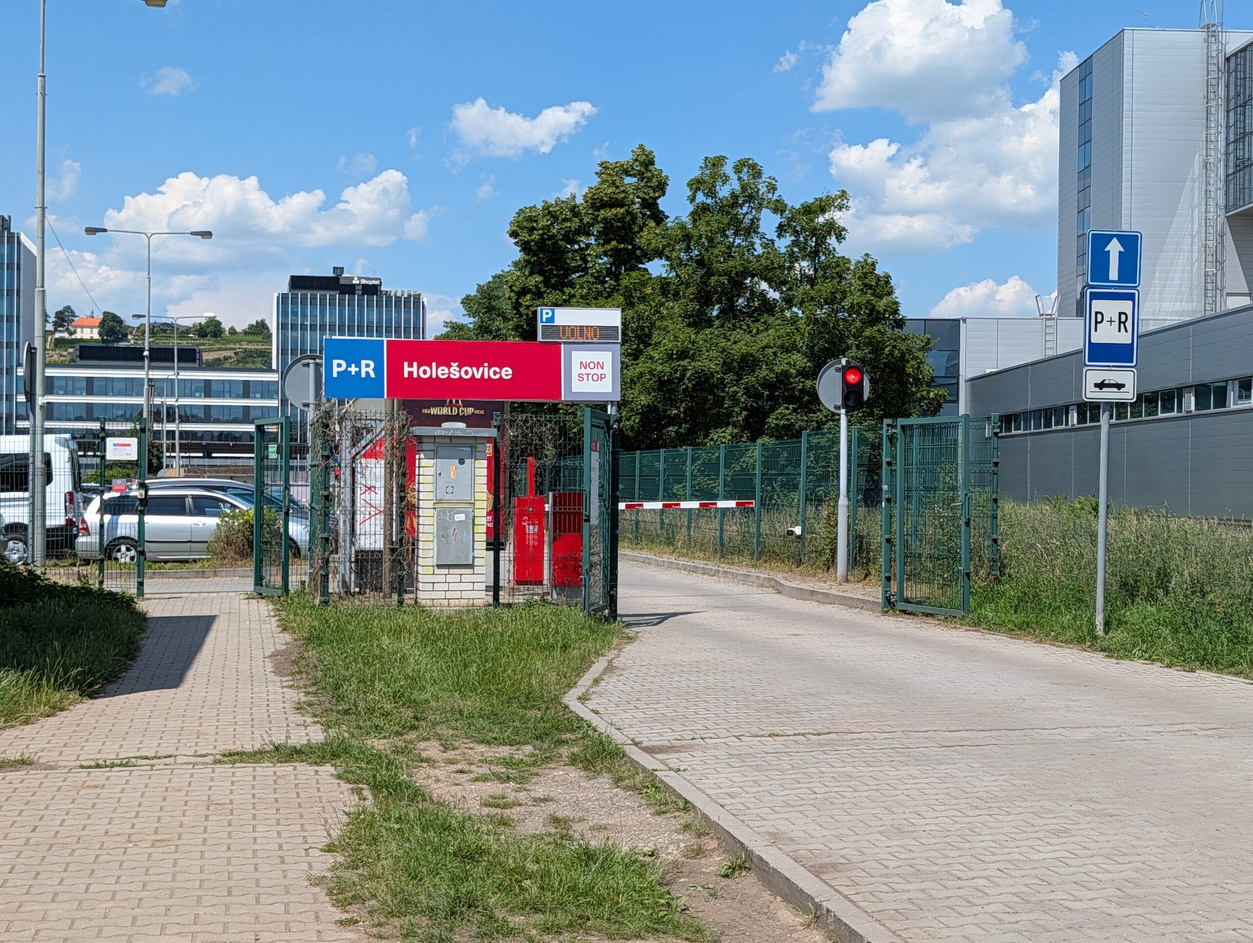 Einfahrt des P+R-Parkplatzes Holešovice in Prag mit Schranke, Kassenautomat und P+R-Beschilderung an einem sonnigen Tag.