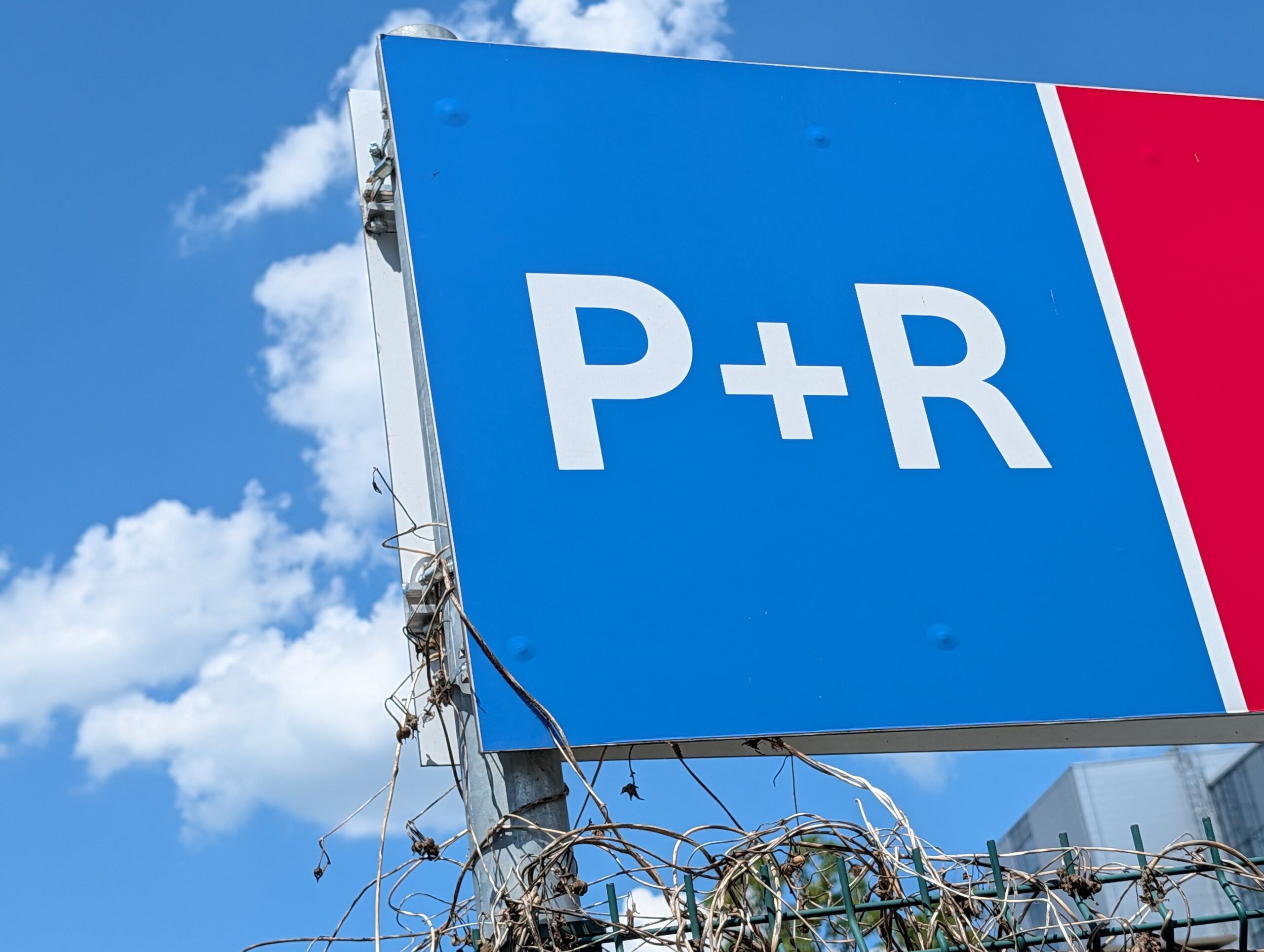 Blaues P+R-Schild an einem Park-and-Ride-Parkplatz in Prag vor blauem Himmel mit weißen Wolken.