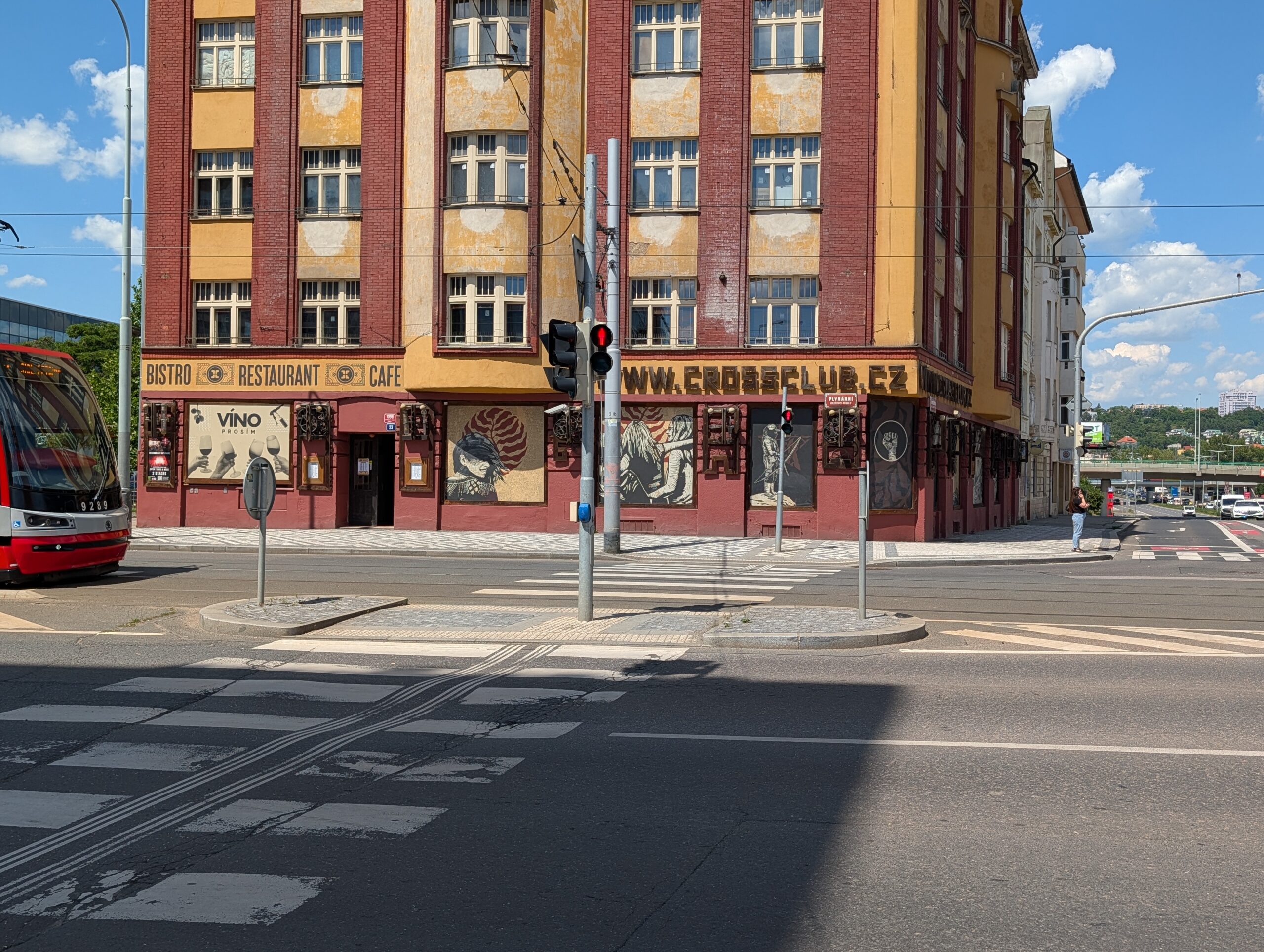 Cross Club in Prag-Holešovice an einer Straßenkreuzung mit Straßenbahn, Fußgängerüberweg und markantem Eckgebäude.
