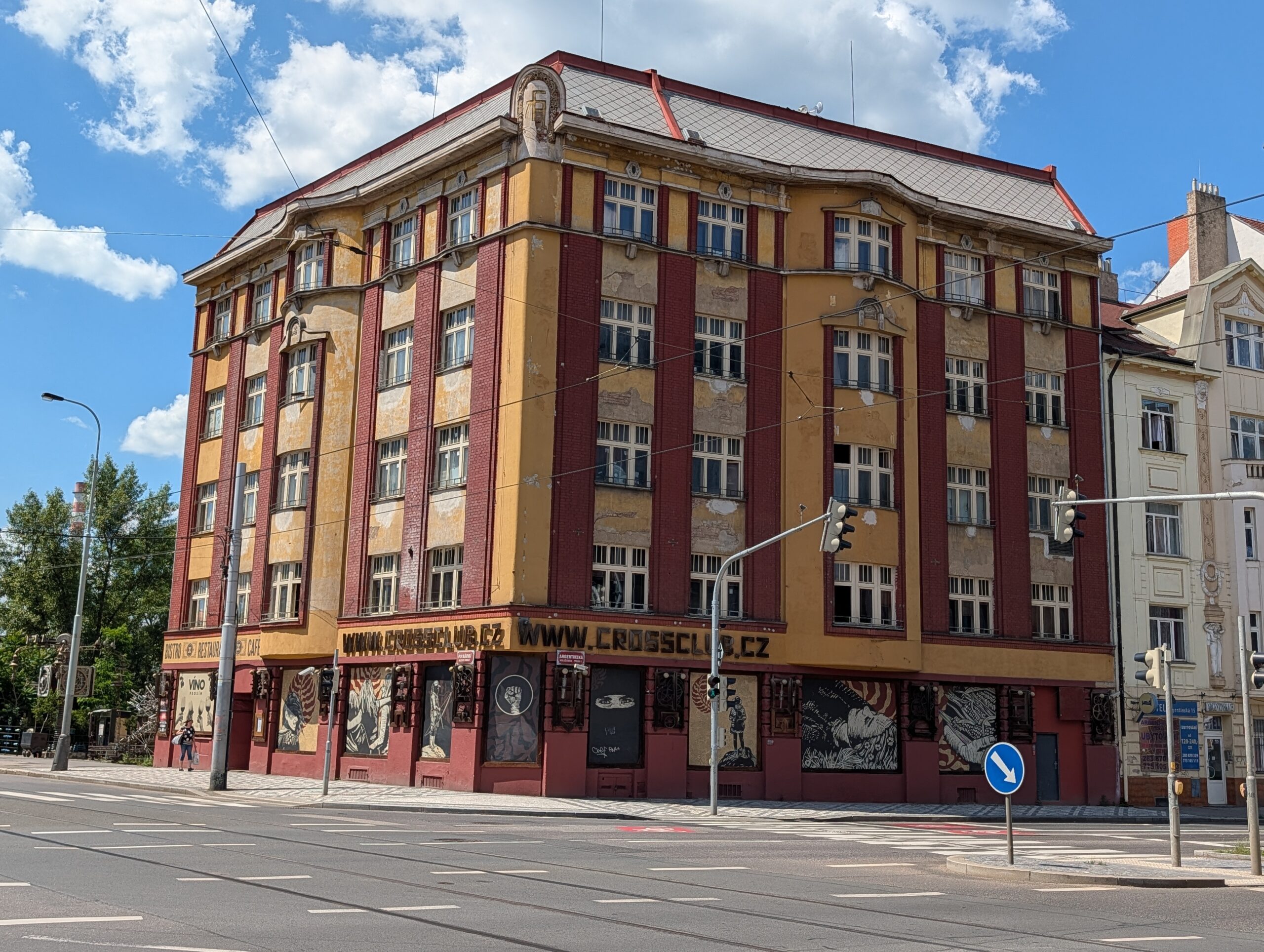 Außenansicht des Cross Club in Prag-Holešovice mit markantem Eckgebäude an einer Straßenkreuzung unter blauem Himmel.