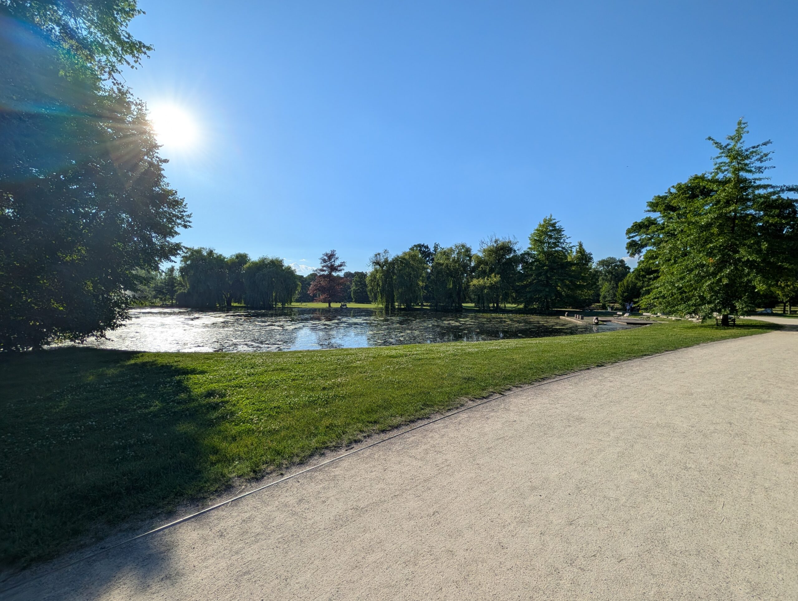 Breiter Spazierweg entlang eines Parkteichs im Königlichen Wildpark Stromovka (Královská obora Stromovka) in Prag.