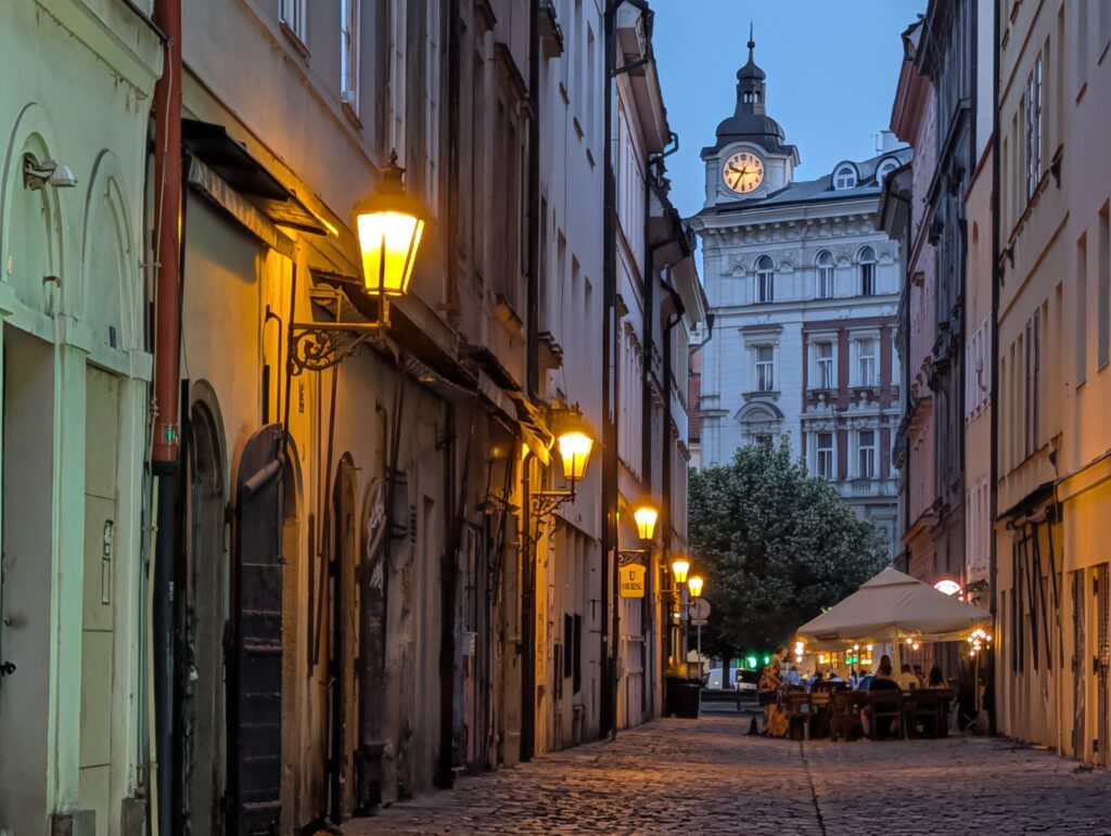 Historische Kopfsteinpflastergasse mit Laternen in der Prager Altstadt bei Abenddämmerung.