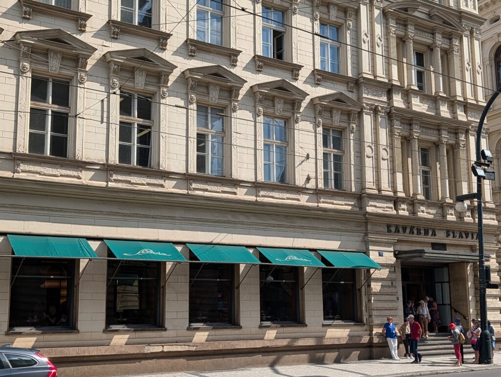 Historische Fassade des Café Slavia in Prag mit grünen Markisen und Personen vor dem Eingang